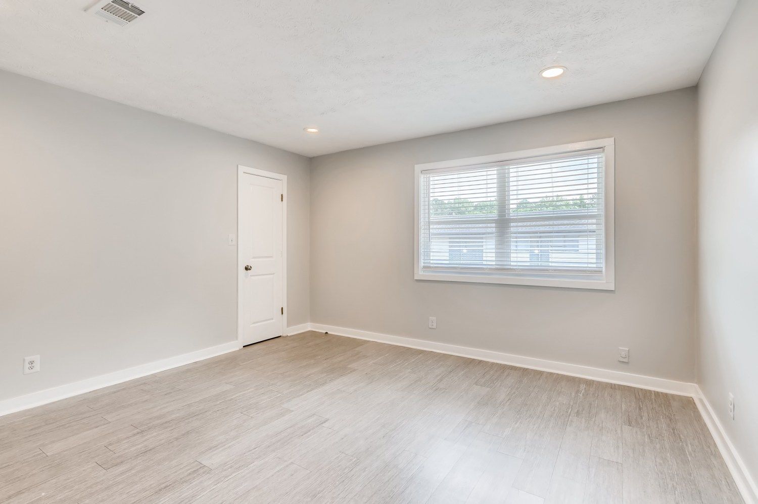 Empty light-gray bedroom with white trim, window blinds, and a closed door.