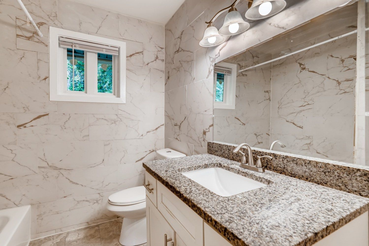 Modern bathroom with marble-look walls, granite vanity, mirror, and window light