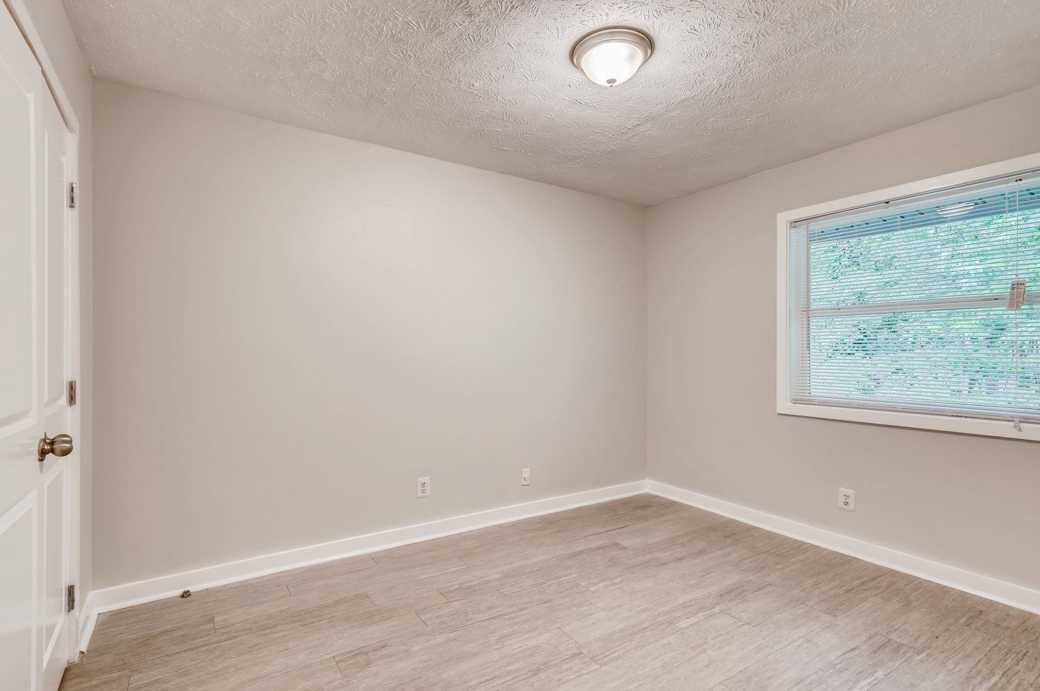 Empty beige bedroom with carpet, window blinds, and ceiling light