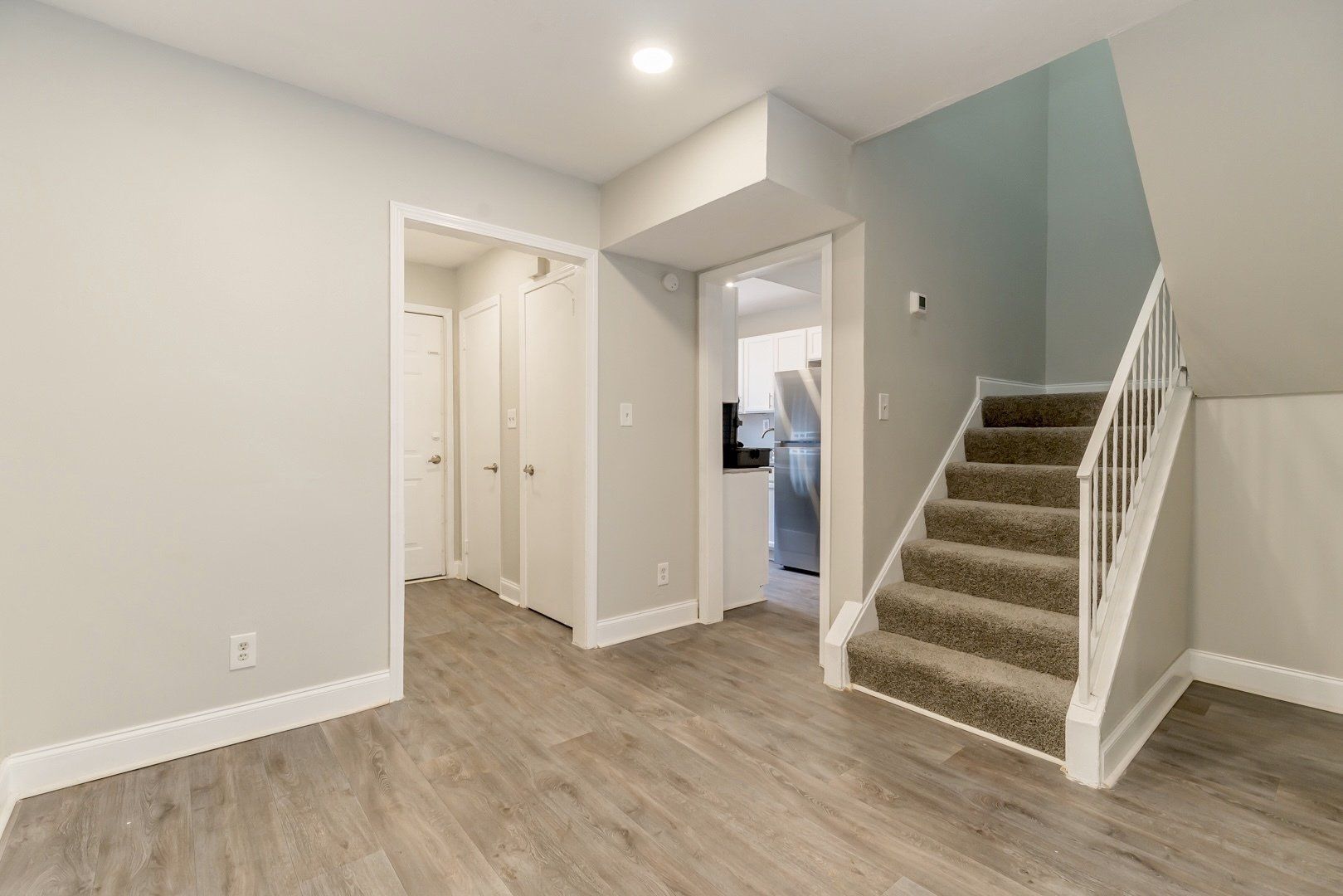 Empty hallway with stairs, white walls, and wood-look flooring in a modern home