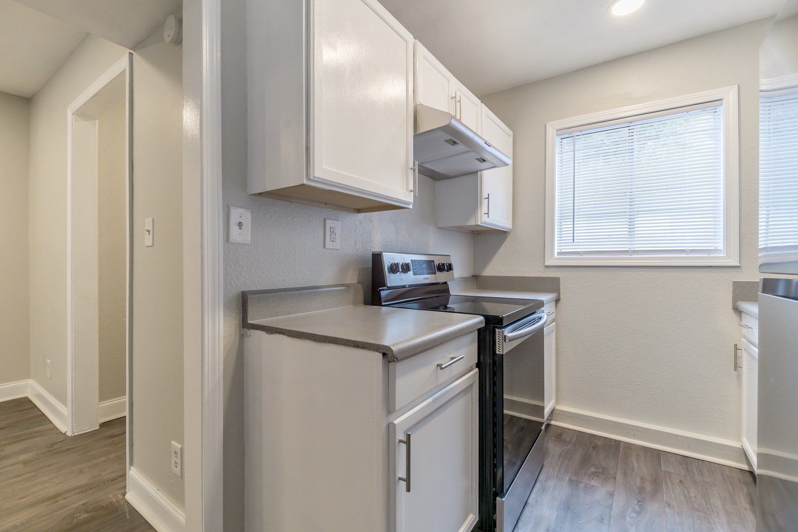 Small kitchen nook with white cabinets, stainless stove, and a window with blinds