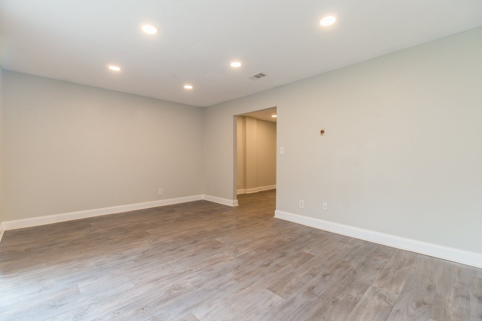 Empty modern room with light gray walls, wood-look flooring, and recessed ceiling lights.