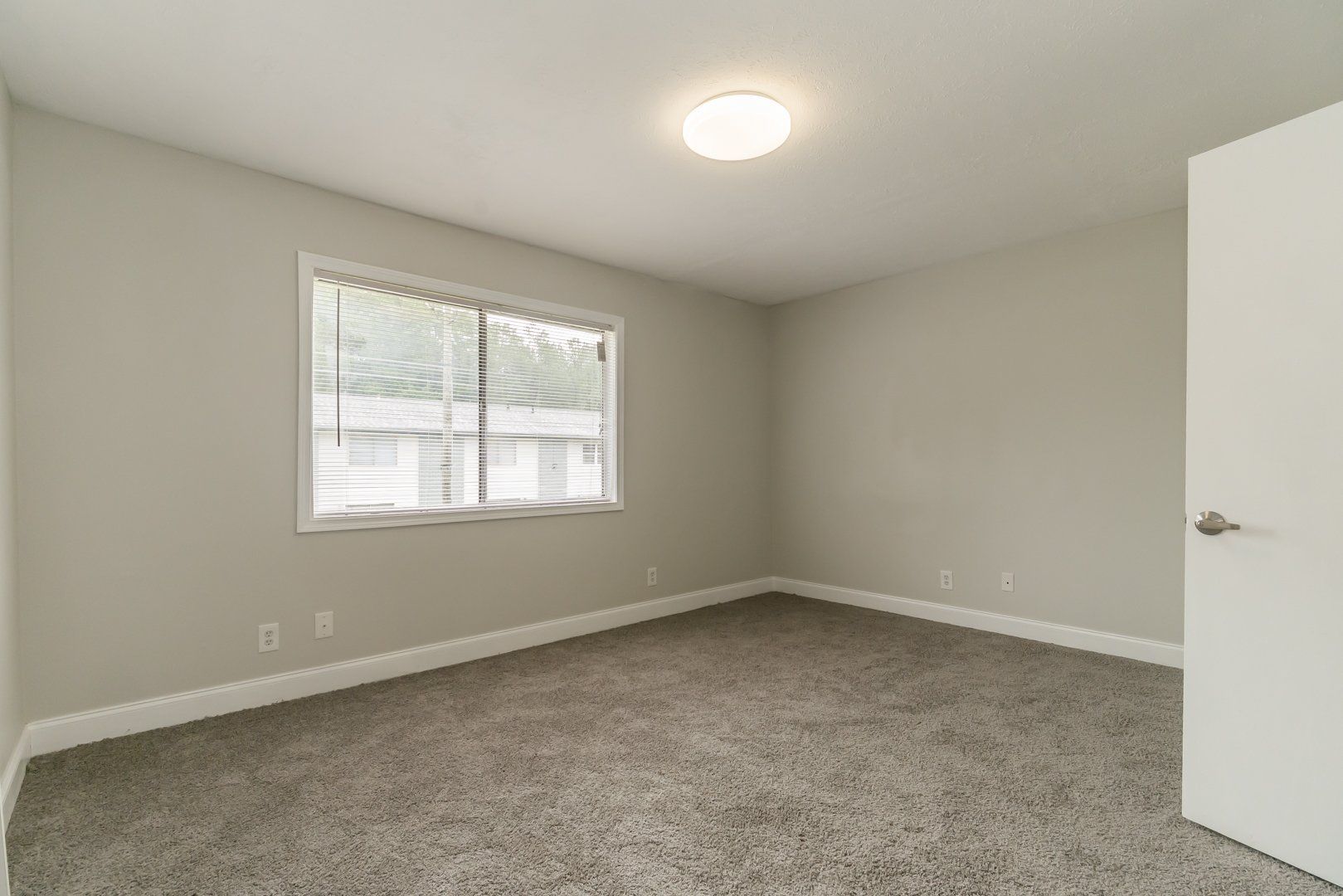 Empty beige bedroom with carpet, window, and open white door