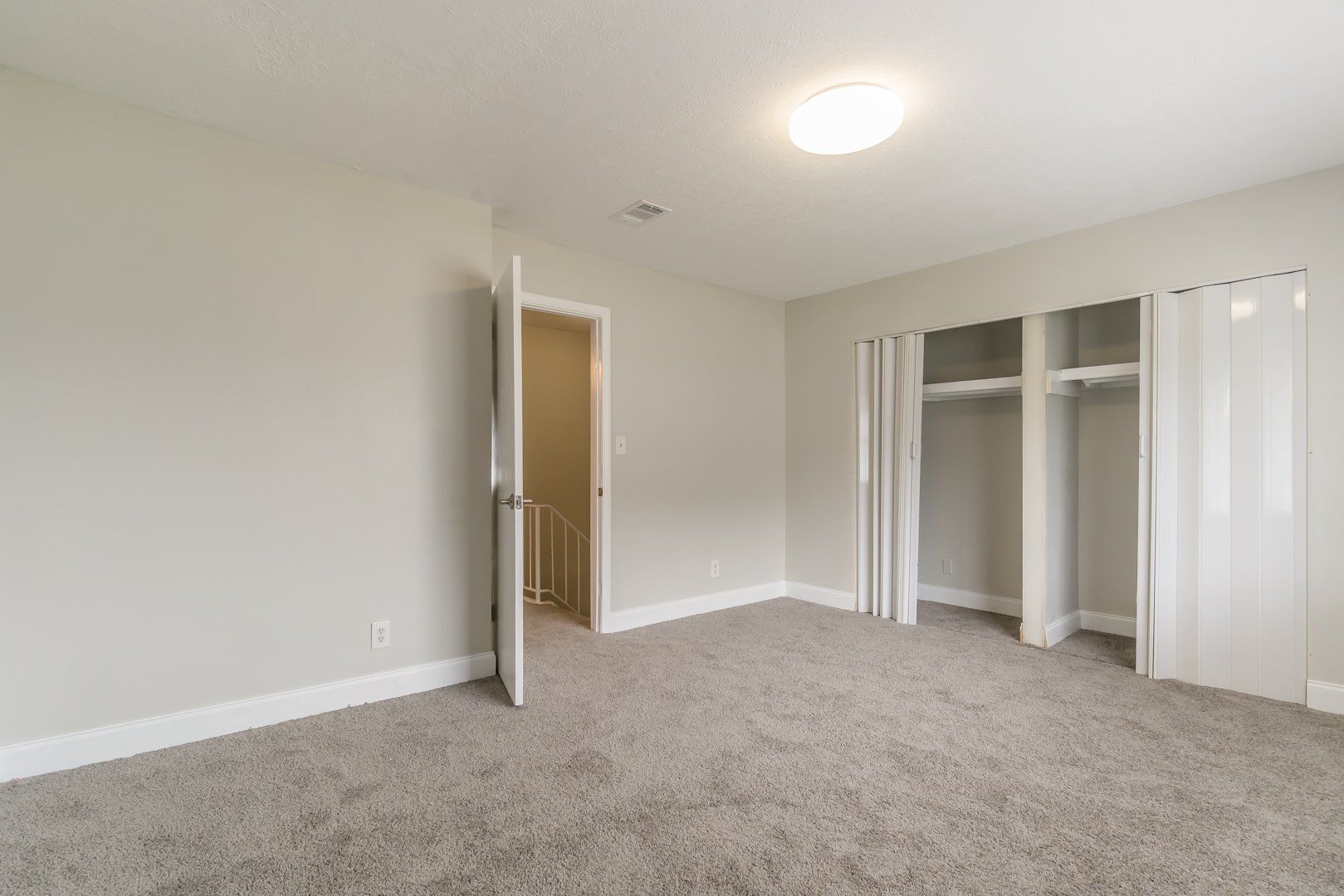 Empty beige bedroom with carpet, open door, and closet with sliding doors