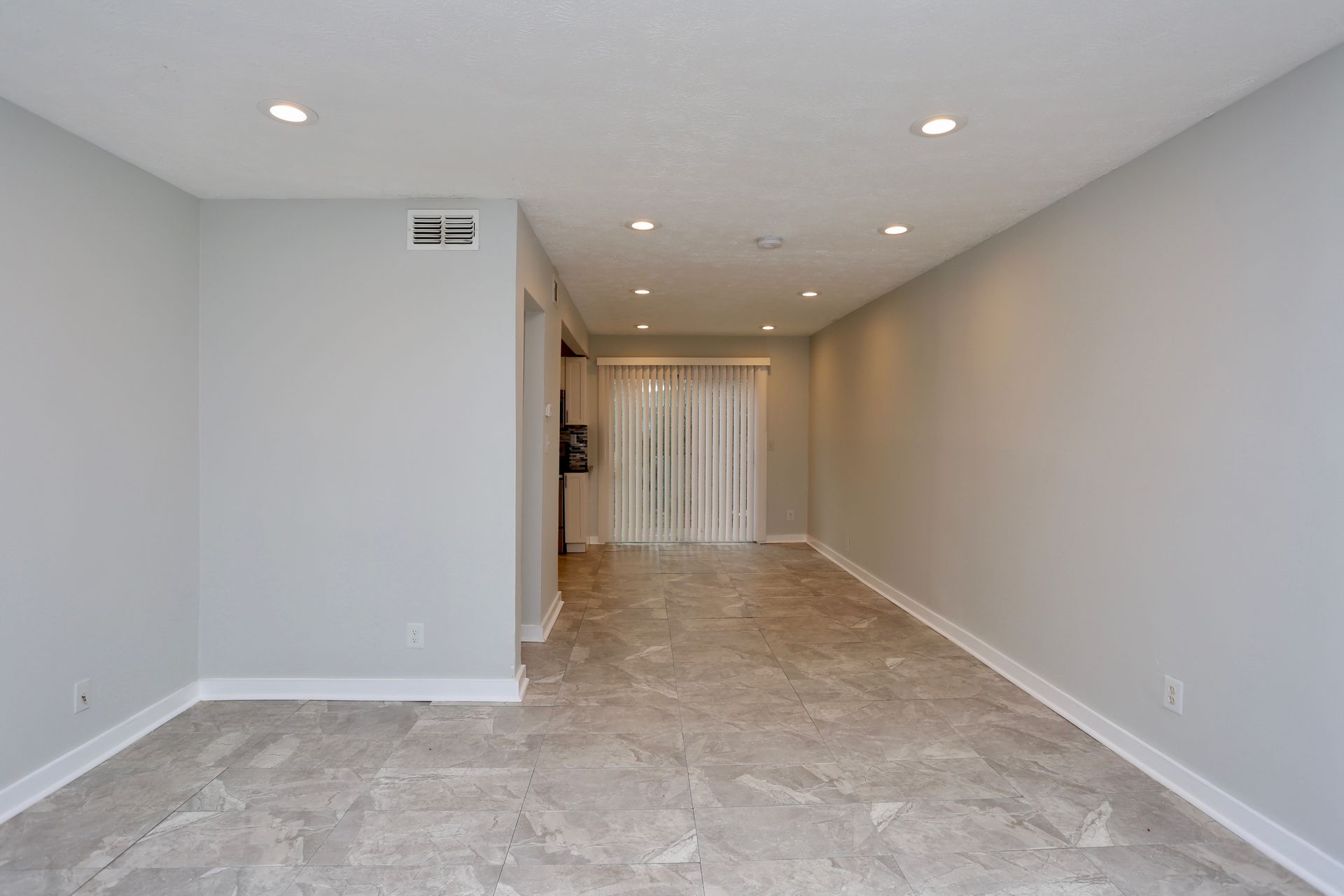 Empty beige hallway with tile floor, recessed lights, and curtained doorway at the far end