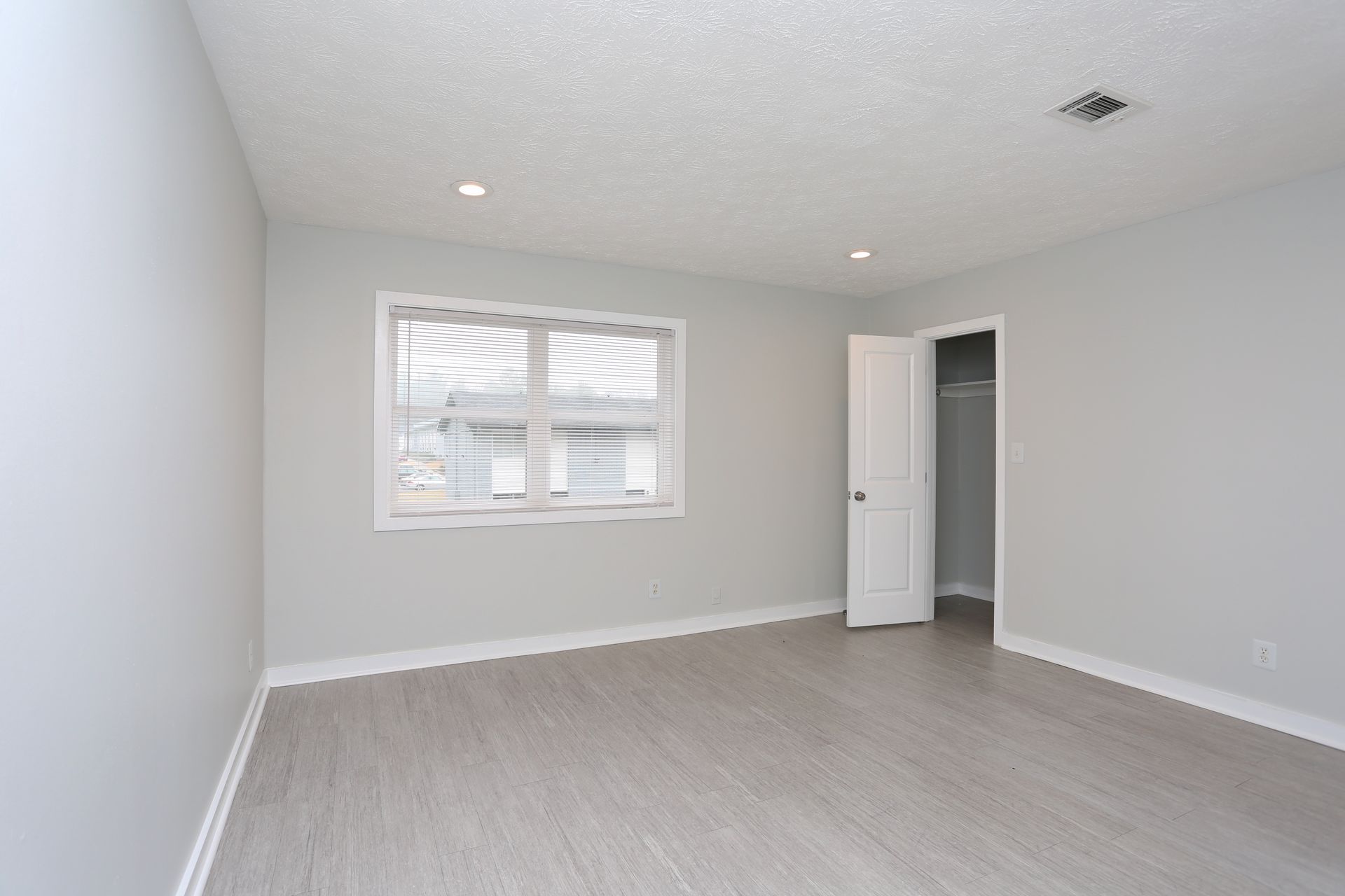 Empty light-gray bedroom with white trim, window blinds, and an open closet door