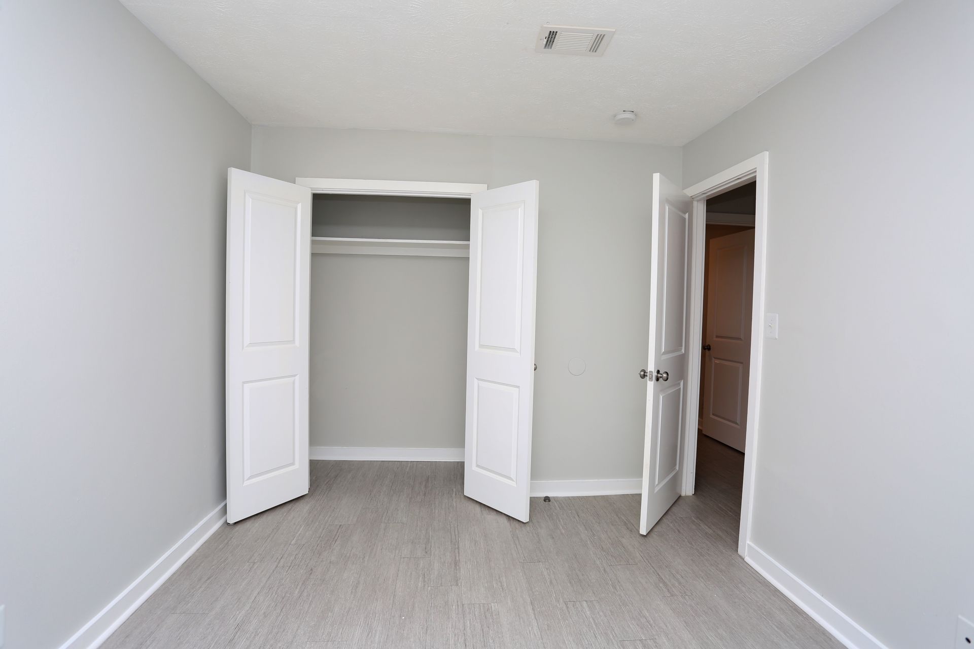 Empty bedroom with open closet and open door to hallway, white walls and light carpet