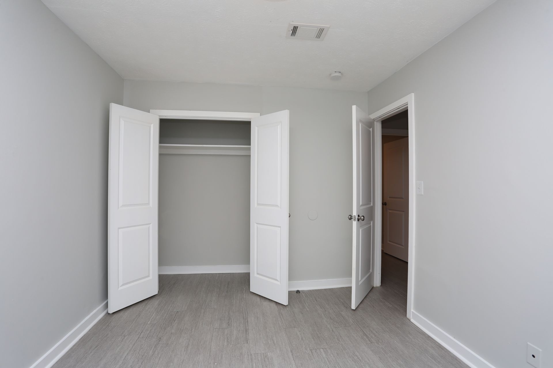 Empty white bedroom with open closet doors and an open door to a hallway