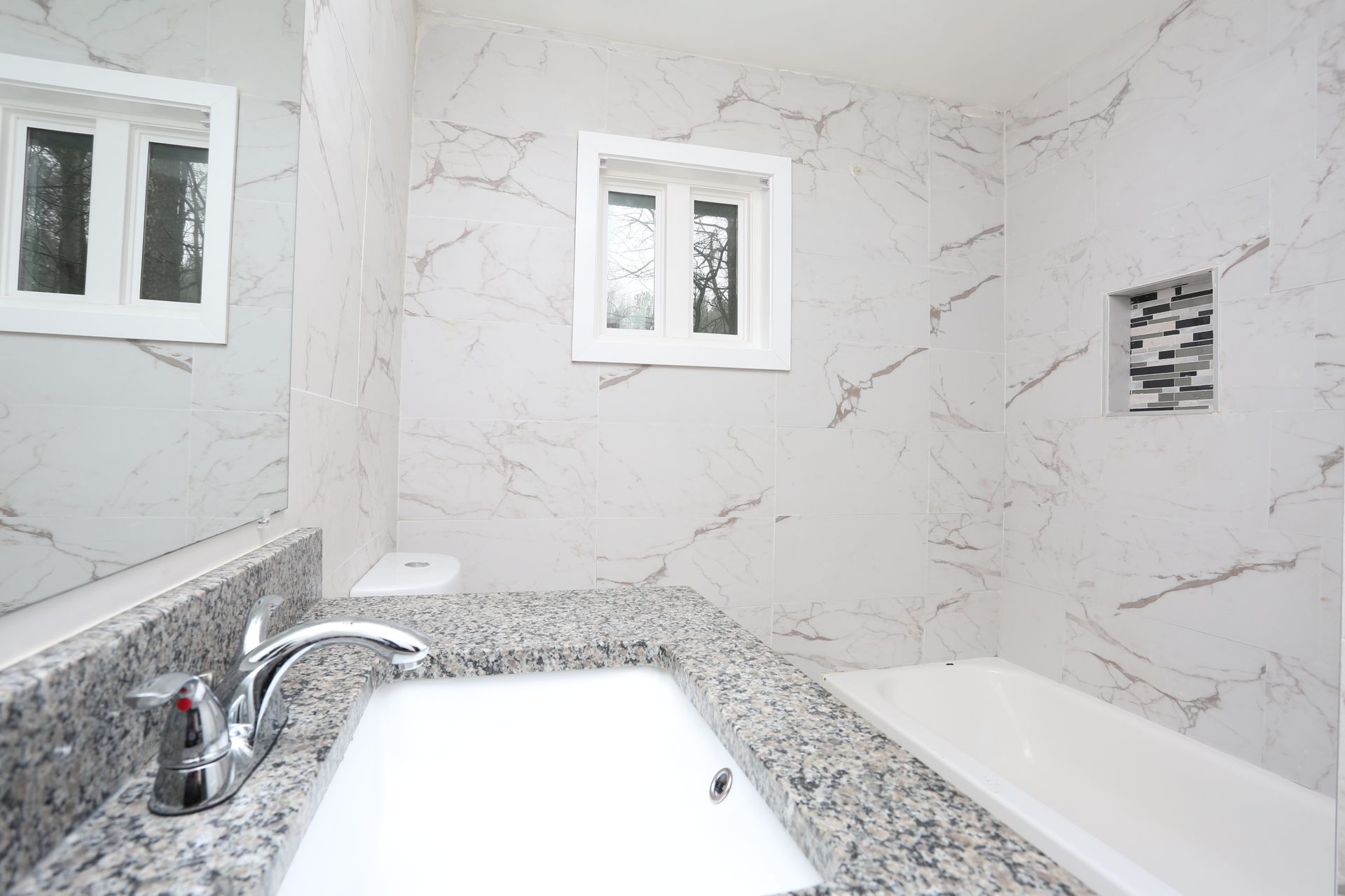 Modern white bathroom with marble-pattern tile, granite sink counter, and small windows