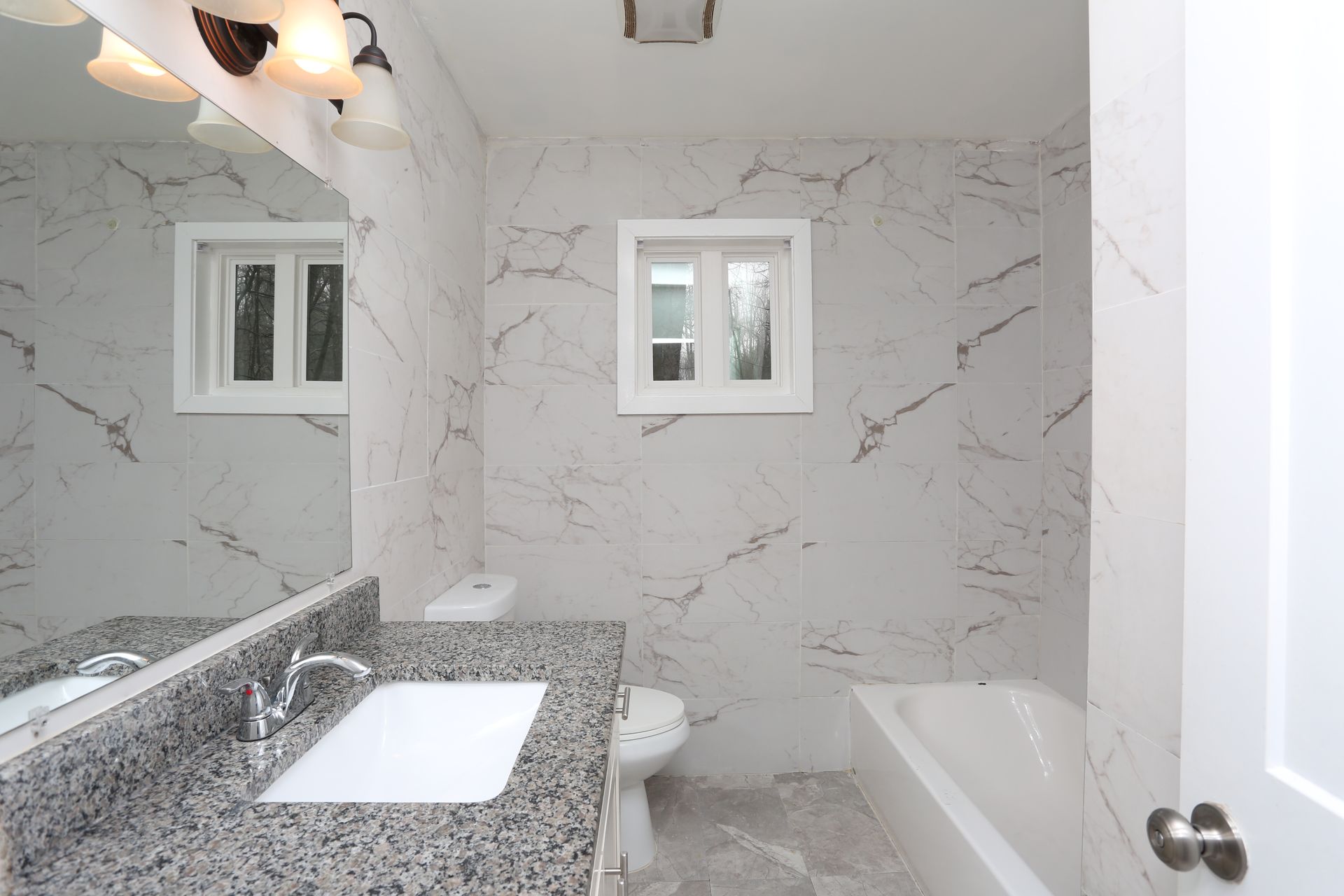 Bright marble bathroom with large mirror, white vanity, window, and bathtub