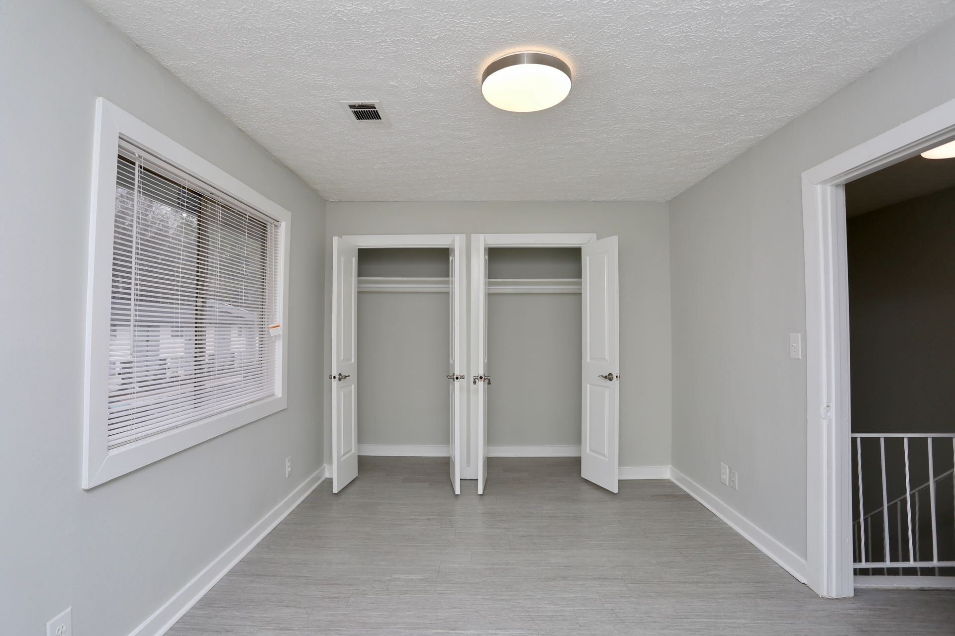Empty gray bedroom with open closet doors, a window, and a ceiling light