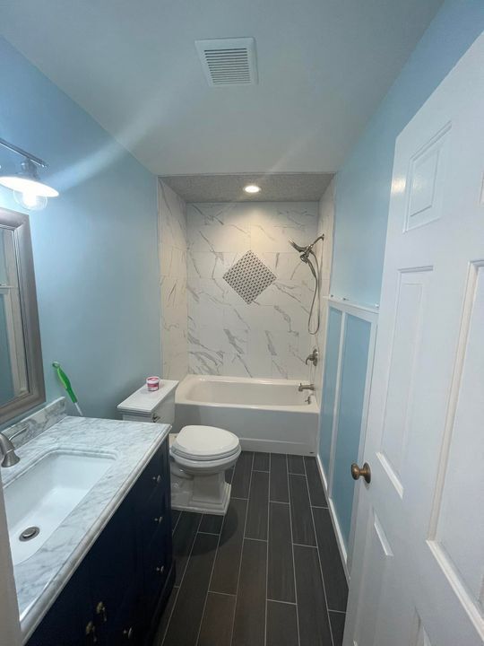Bathroom with blue walls, white tub, dark tile floor, vanity, and toilet.