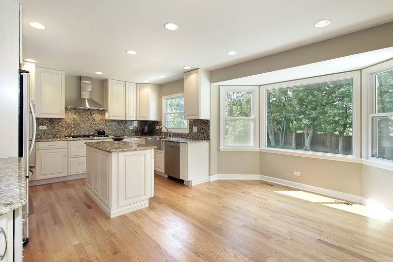 Bright kitchen with light wood floors, white cabinets, granite countertops, and bay window.