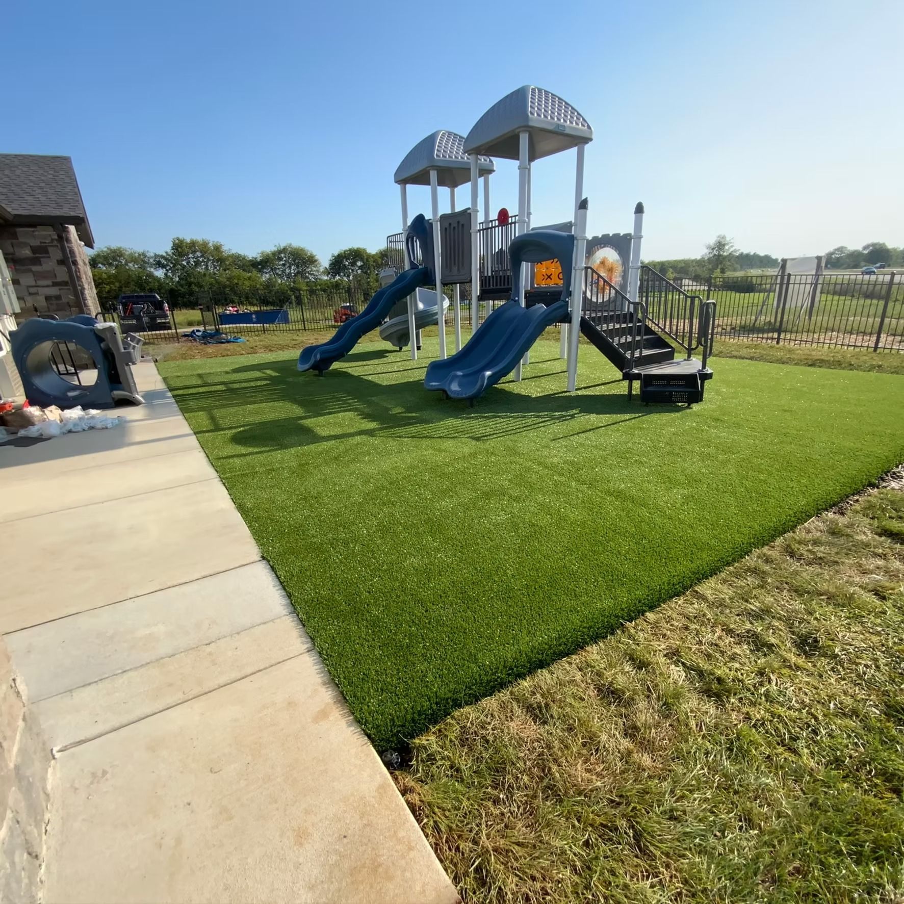 Playground with blue slides, gray structures, and green artificial turf.