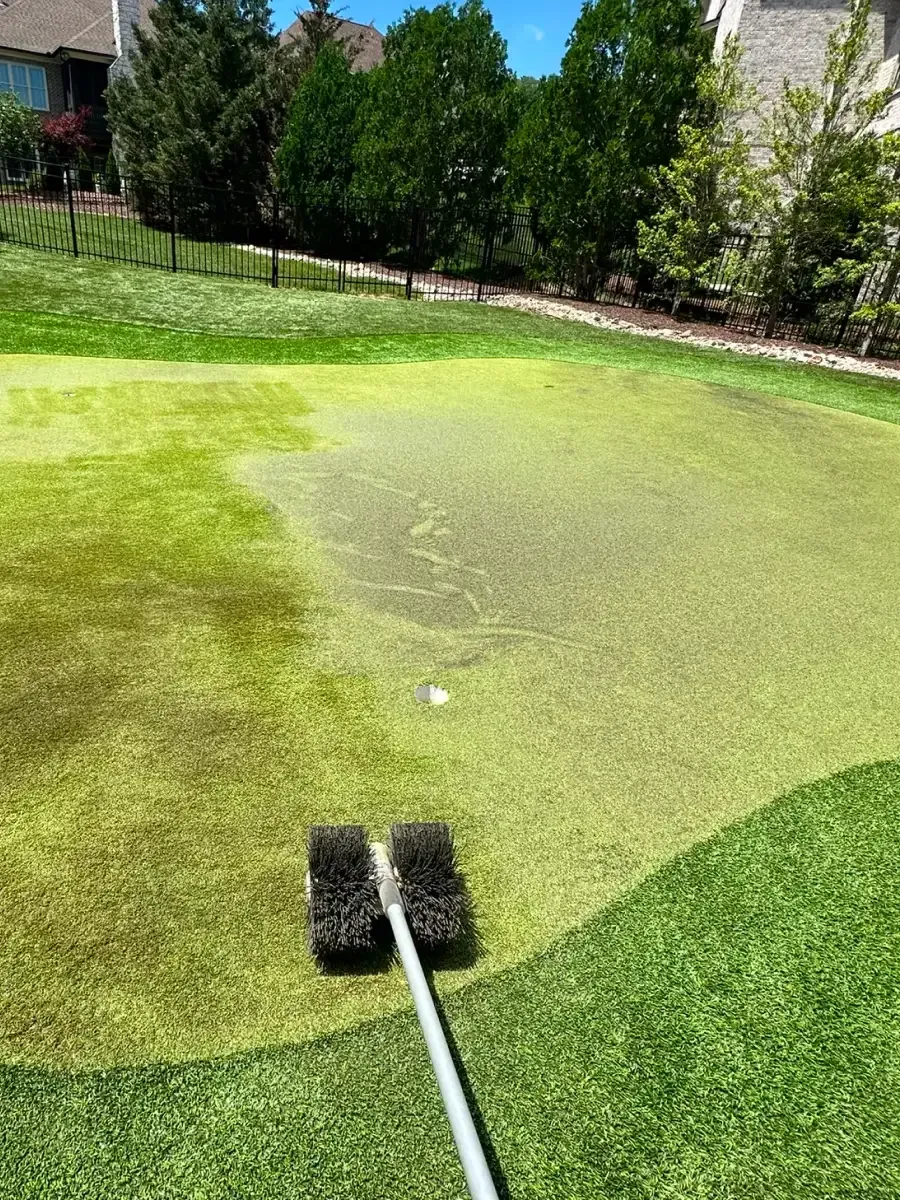 A person is cleaning a golf green with a brush. The green is partly covered in algae.