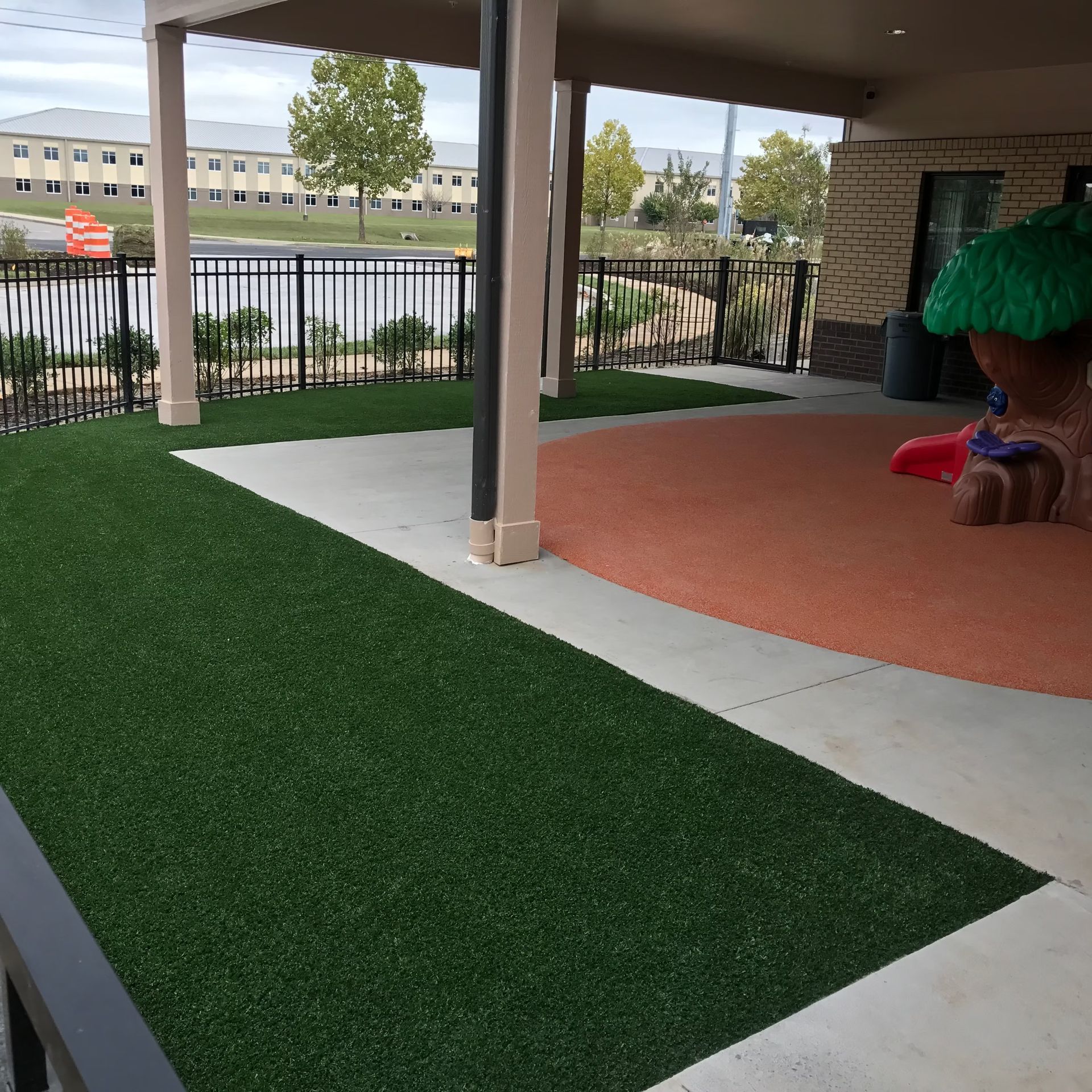Covered outdoor play area with green turf, tan concrete, and a play structure.