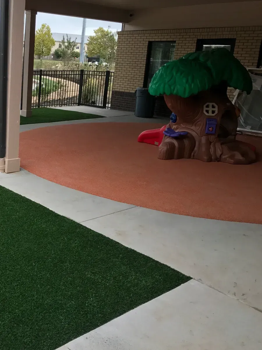Playground area with treehouse structure, artificial turf, and orange-colored flooring.