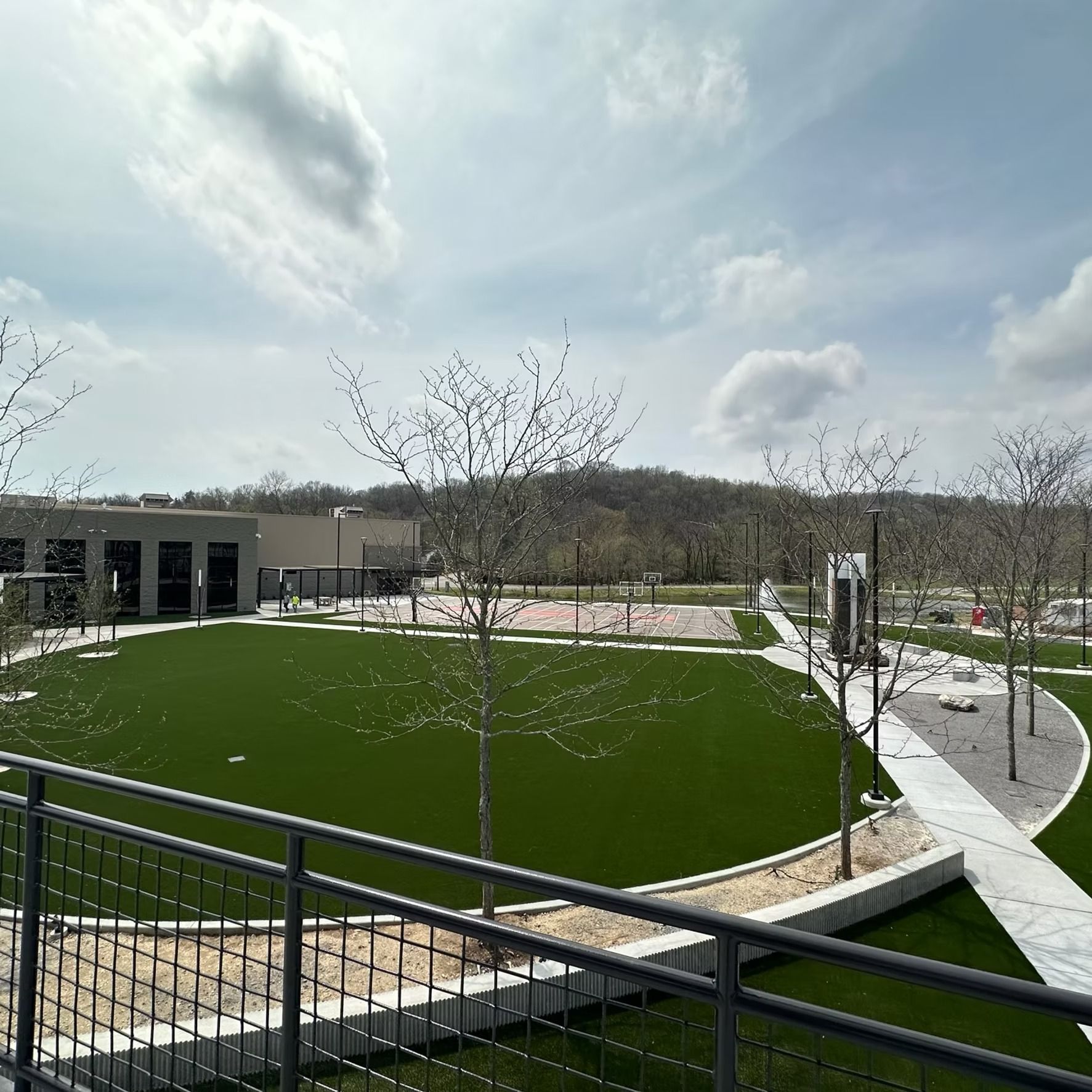 Exterior view of a green lawn and concrete walkways surrounding a building and trees under a cloudy sky.