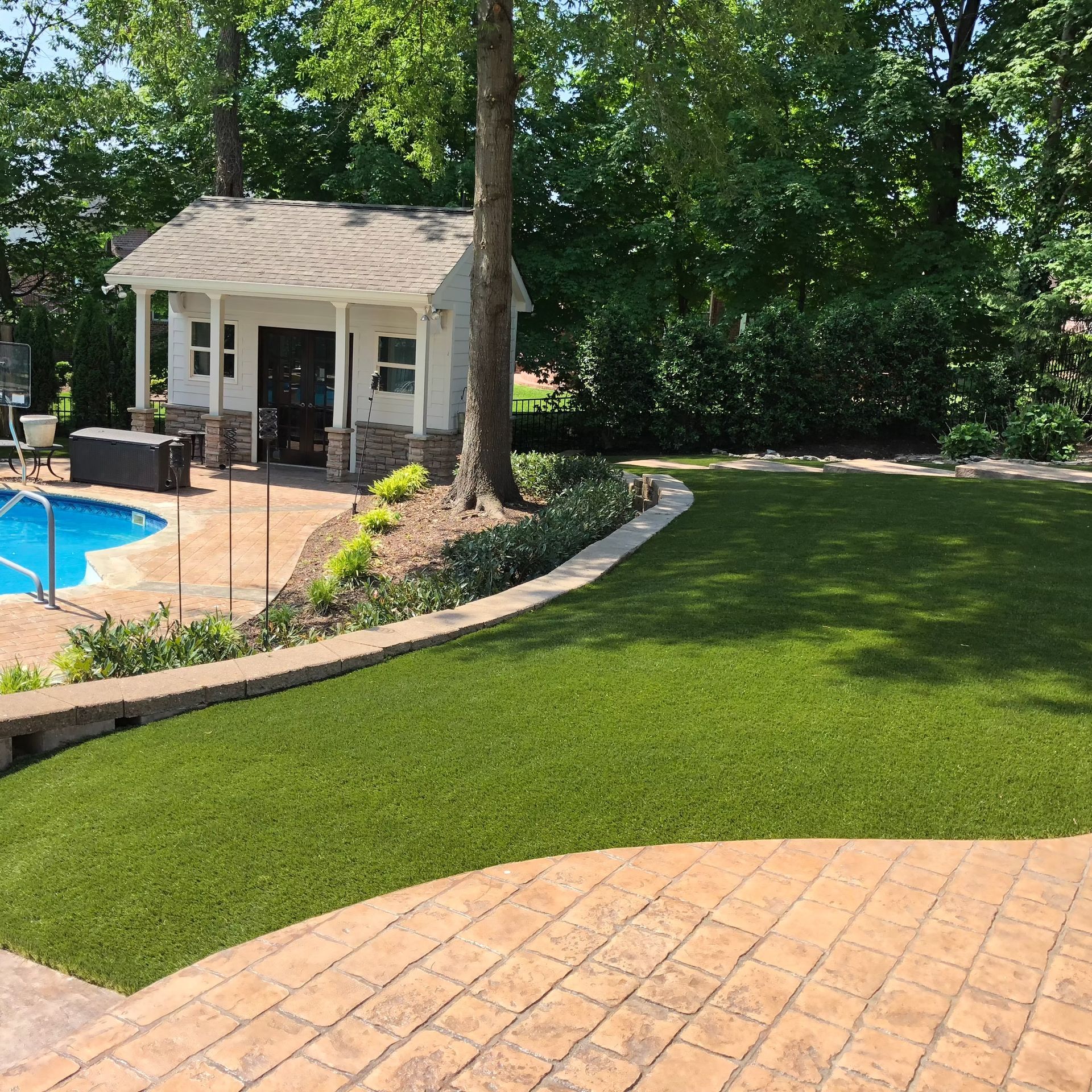 A backyard with a pool, a small white building, and a green lawn.