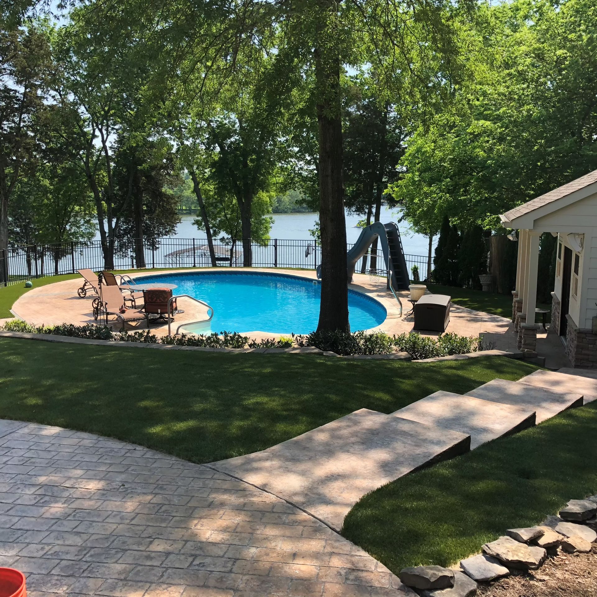Backyard pool with lake view. Blue pool, stamped concrete patio, green grass, trees.