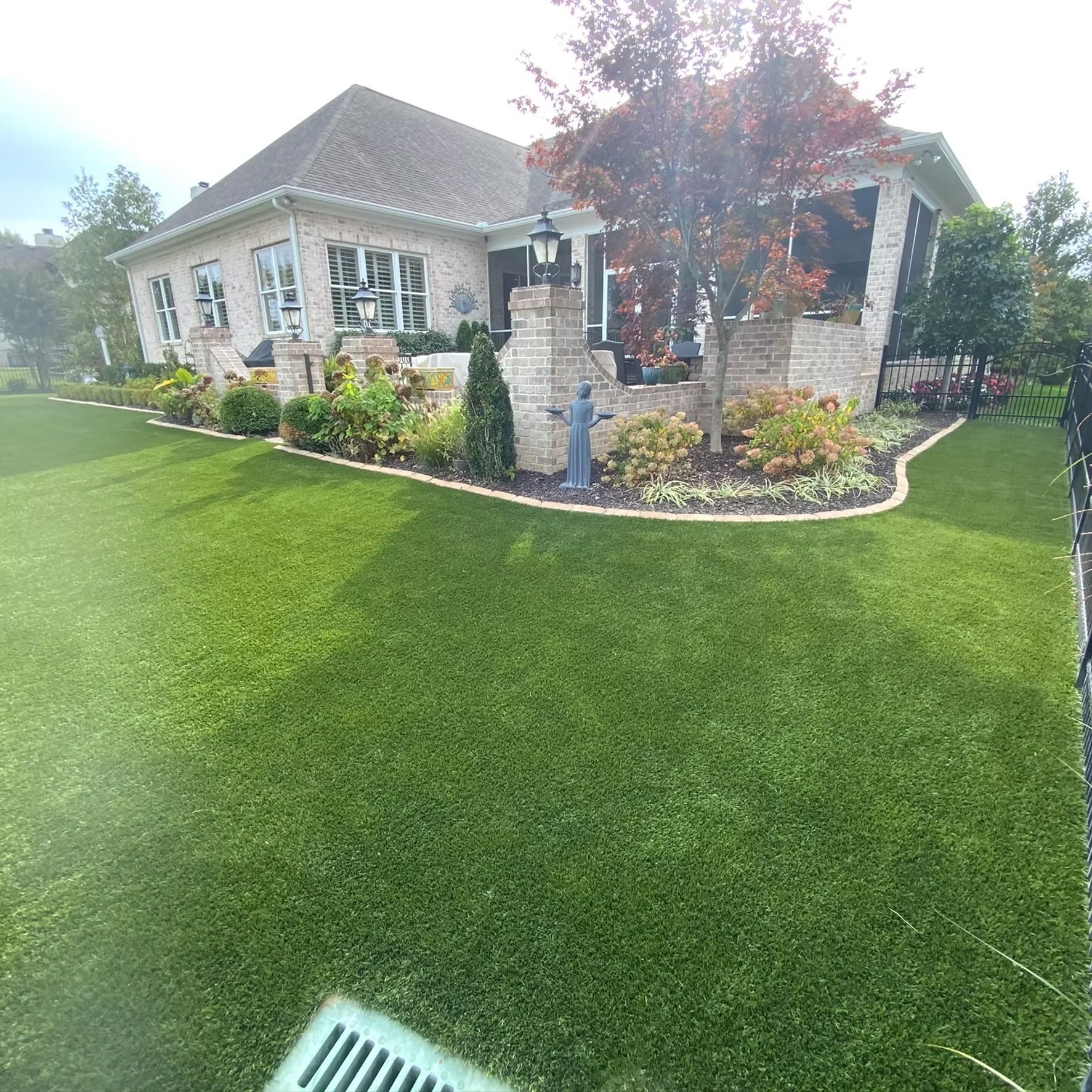 House with brick facade and green lawn, landscaped flowerbeds, and a small tree.