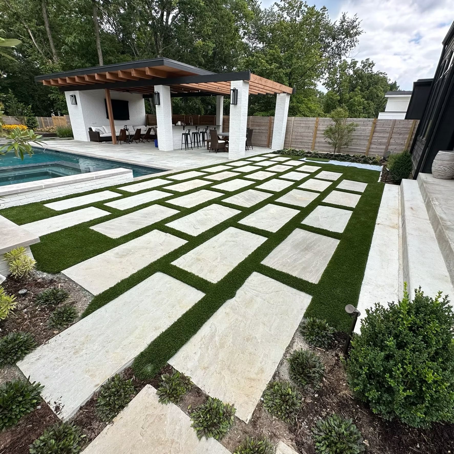 Patio with rectangular concrete pavers and artificial turf leading to a poolside cabana.