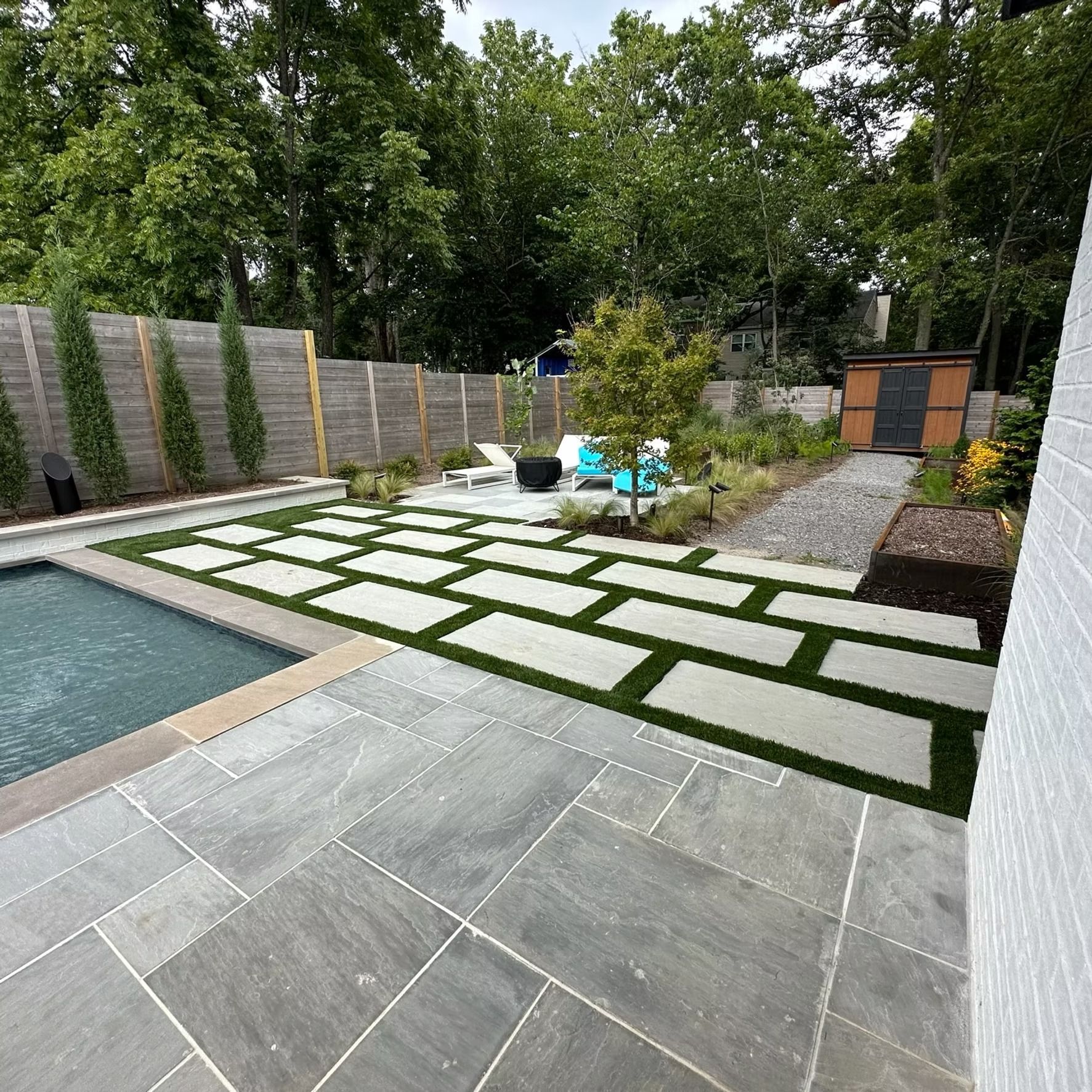 Backyard with pool, stone patio, green grass, and modern landscaping.