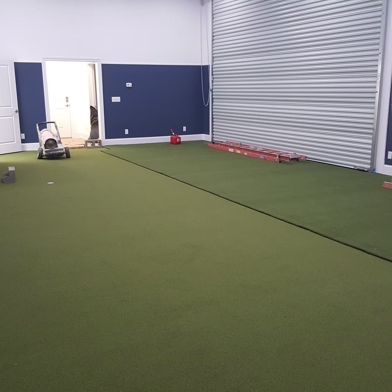 Green indoor sports area with training equipment and a dark blue wall.