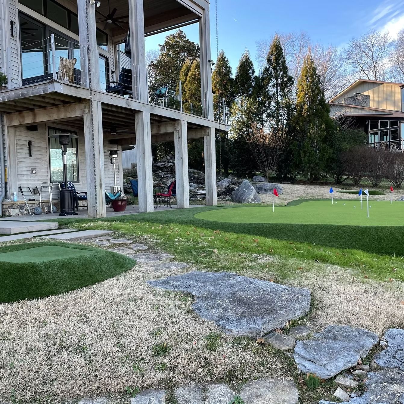 Backyard with a putting green, two-story house, and stone pathway.