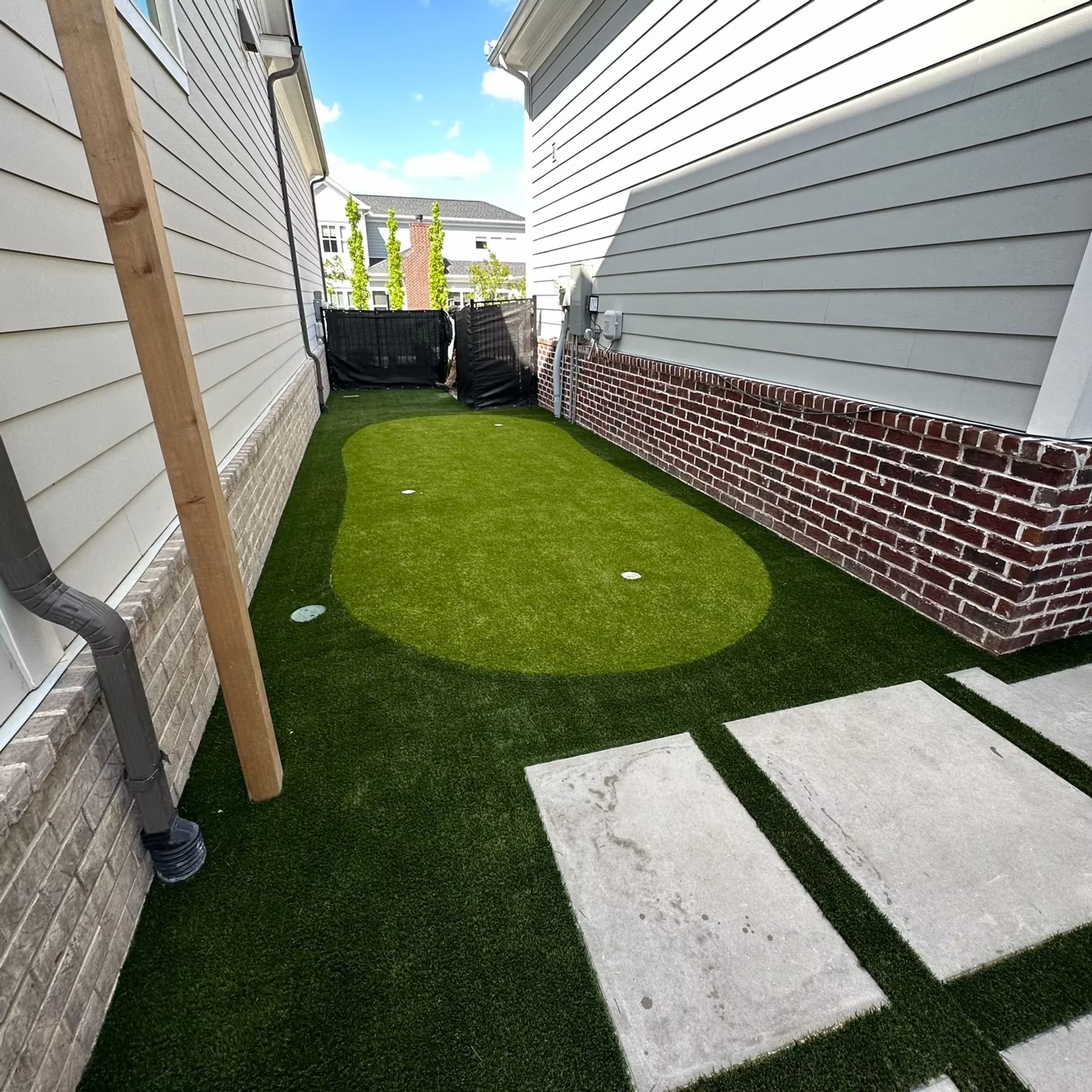 Small backyard with artificial turf, bordered by buildings and a brick wall. Concrete pavers lead to the yard.