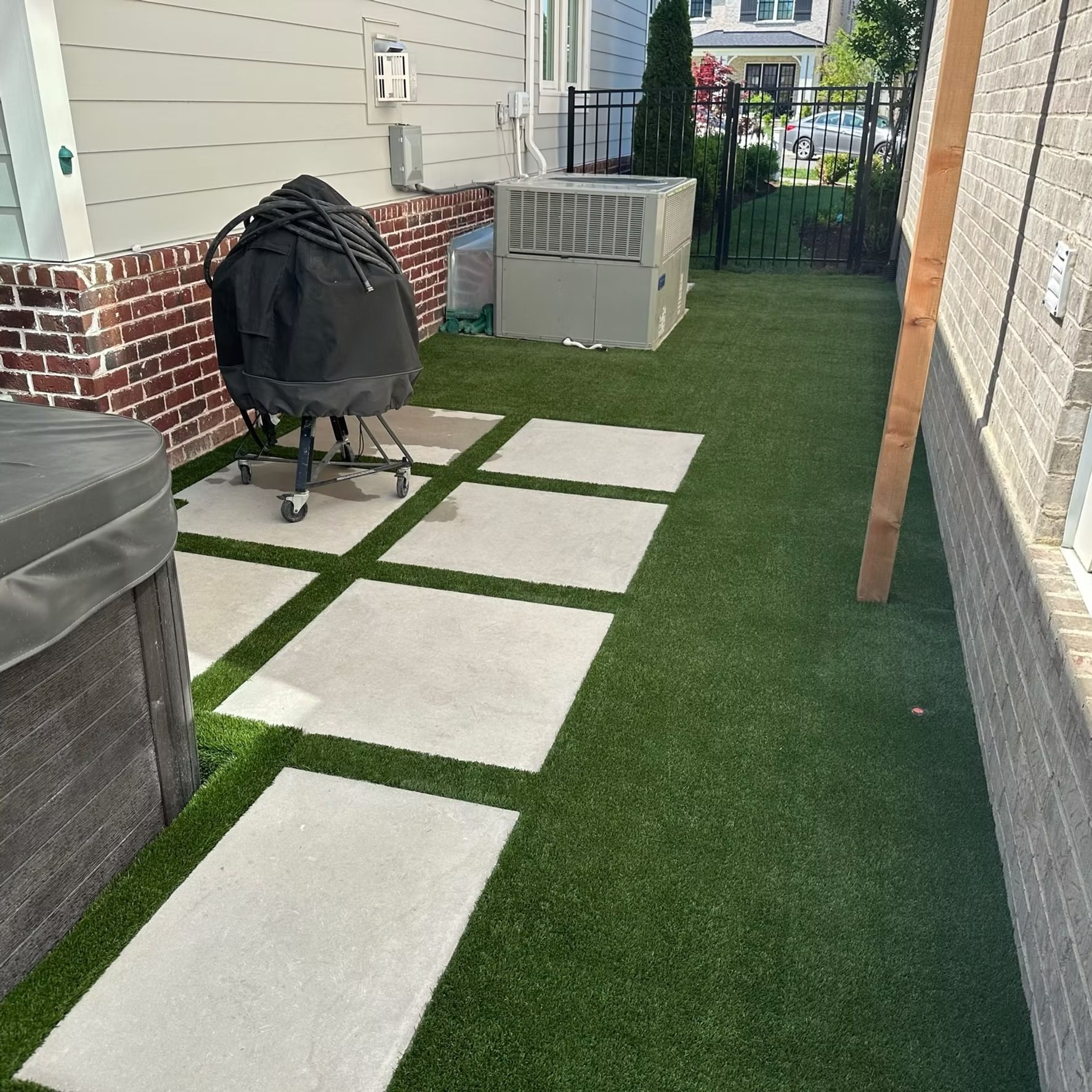 Backyard with artificial grass, concrete pavers, grill, and air conditioning units.