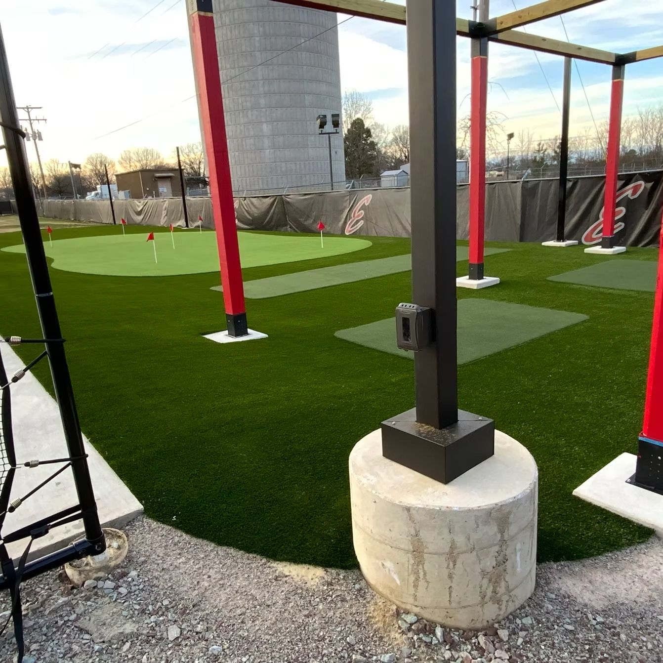 Golf putting green with artificial turf. Red and black structures surround the green. A silo is in the background.