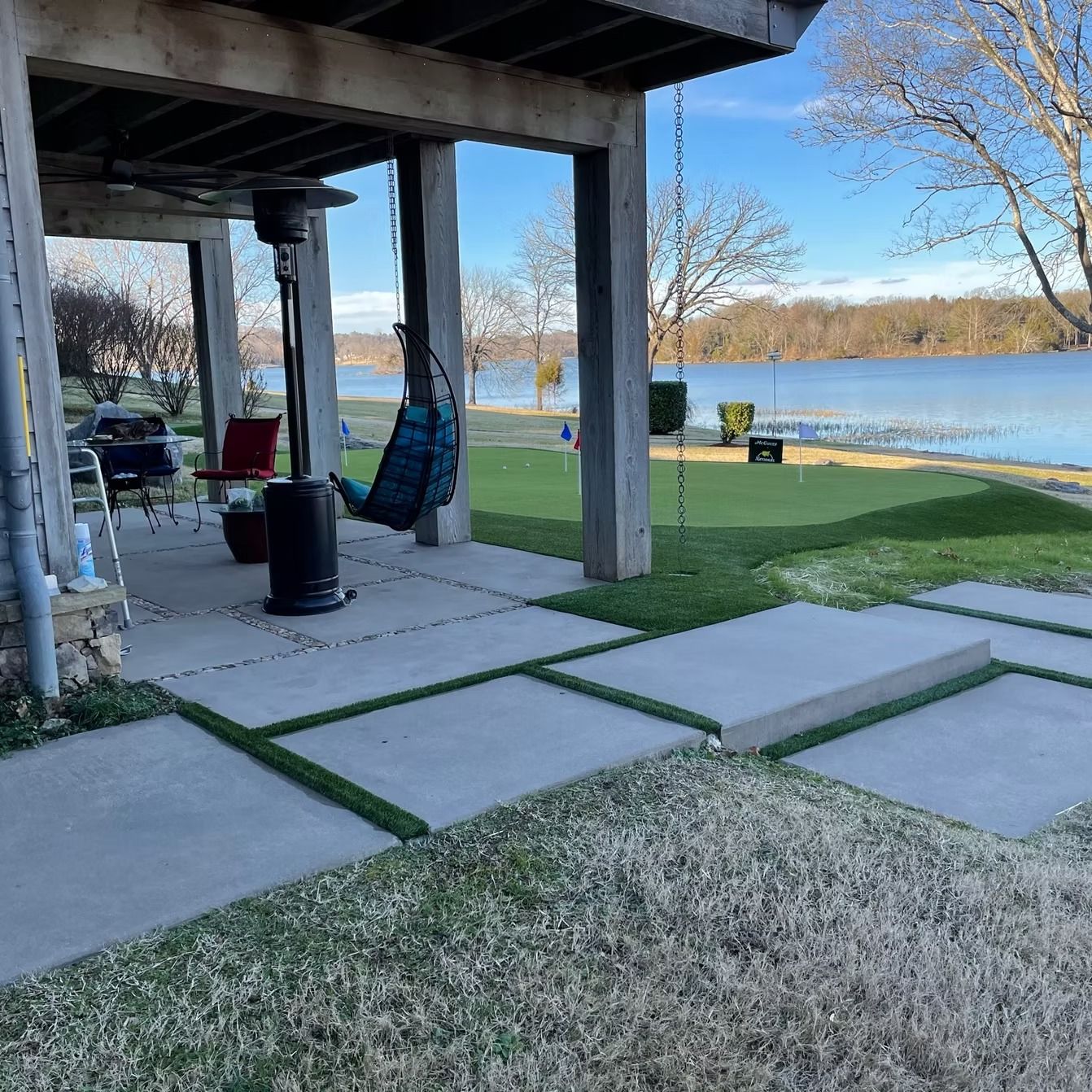 Patio overlooking a lake with gray concrete pavers and green artificial turf.