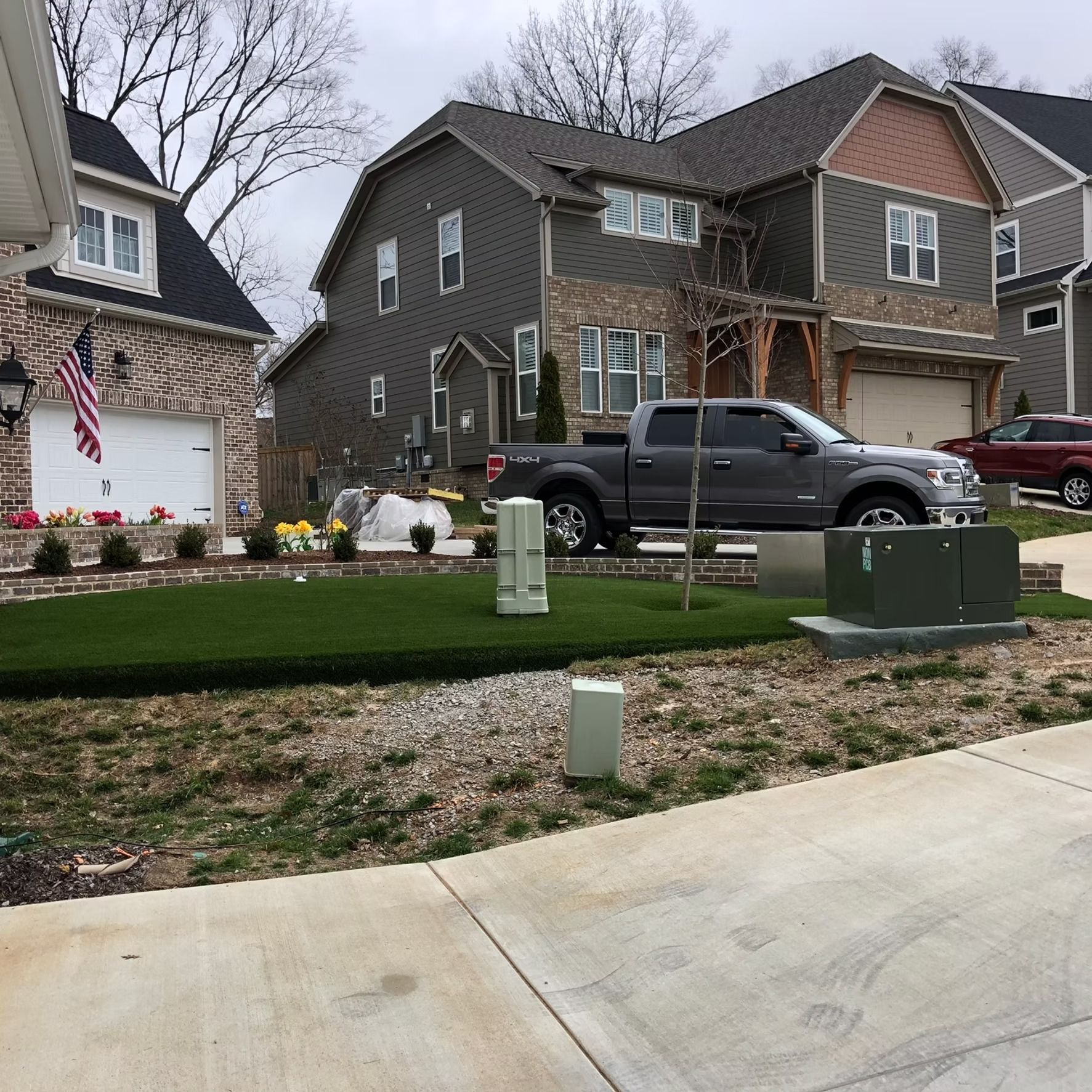 Residential street with houses, a truck, and a grassy yard.