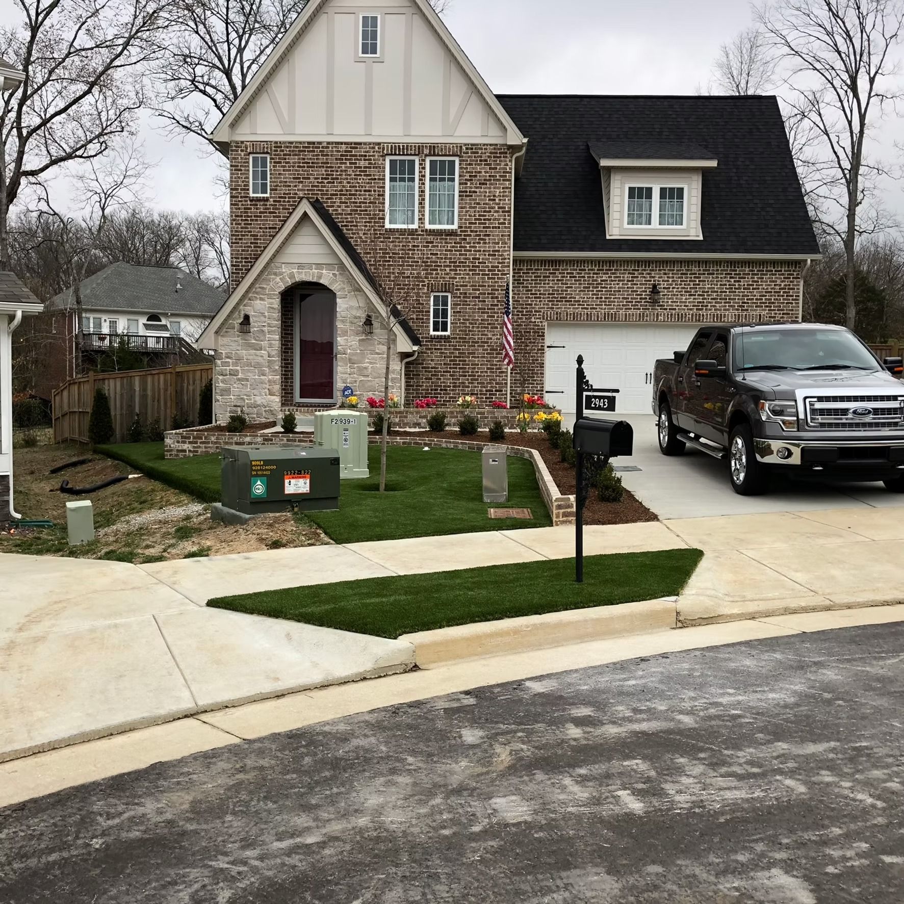 Two-story brick house with a truck parked in the driveway. Landscaped front yard with green grass and flowerbeds.