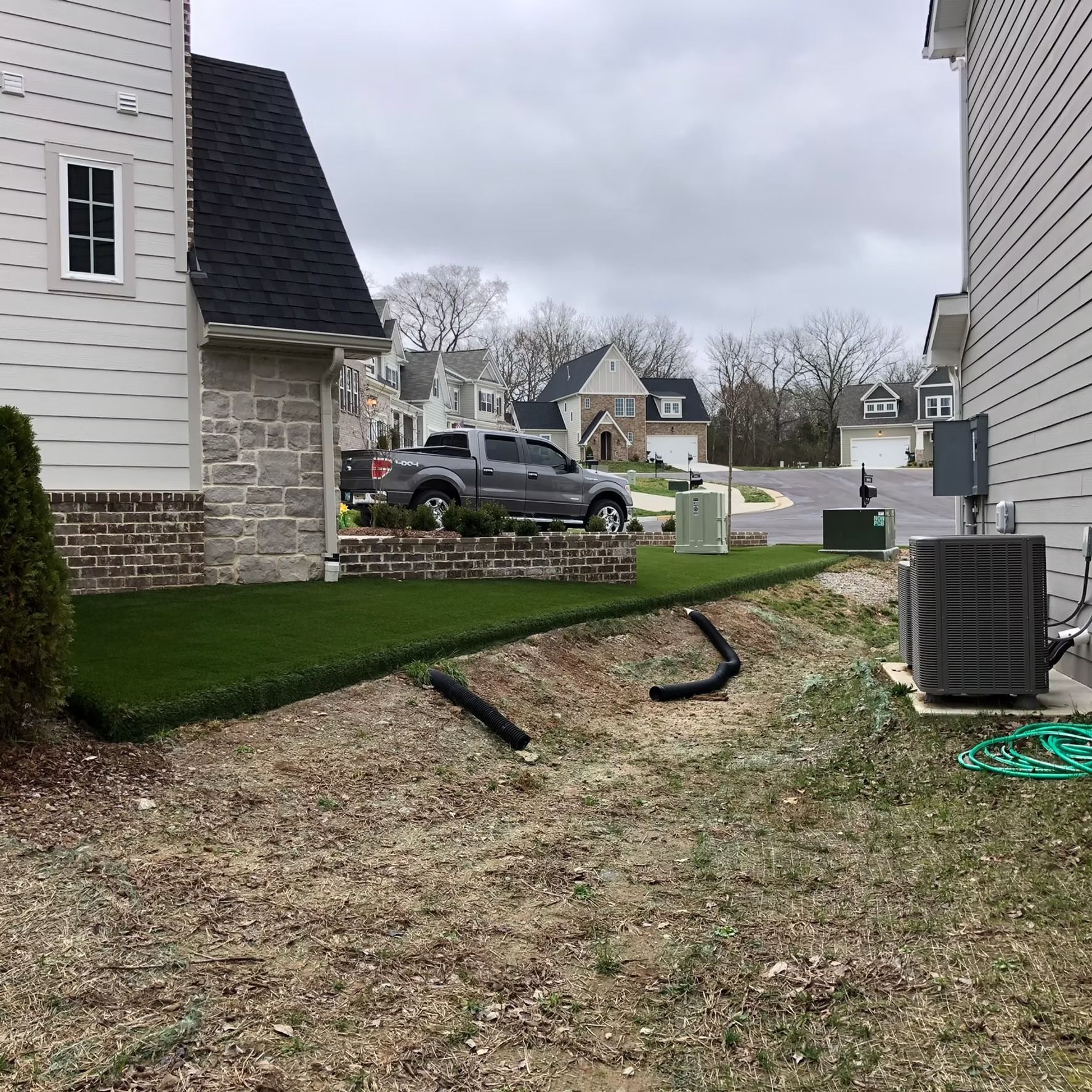 A gray pickup truck parked on a small hill with a green lawn. Houses and a cloudy sky are in the background.