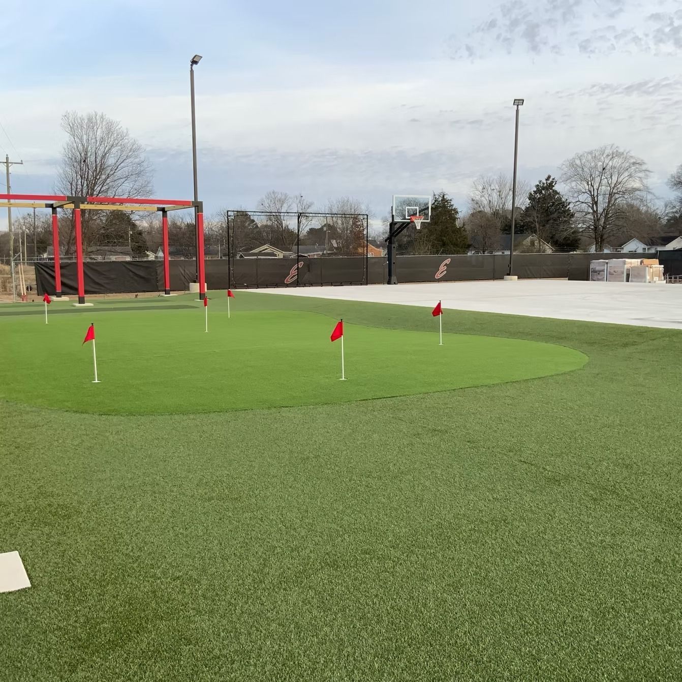 Putting green with red flags; basketball hoop visible in the background.