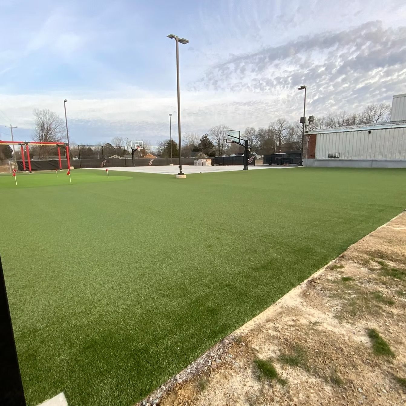 Green turf sports field with light poles and building.