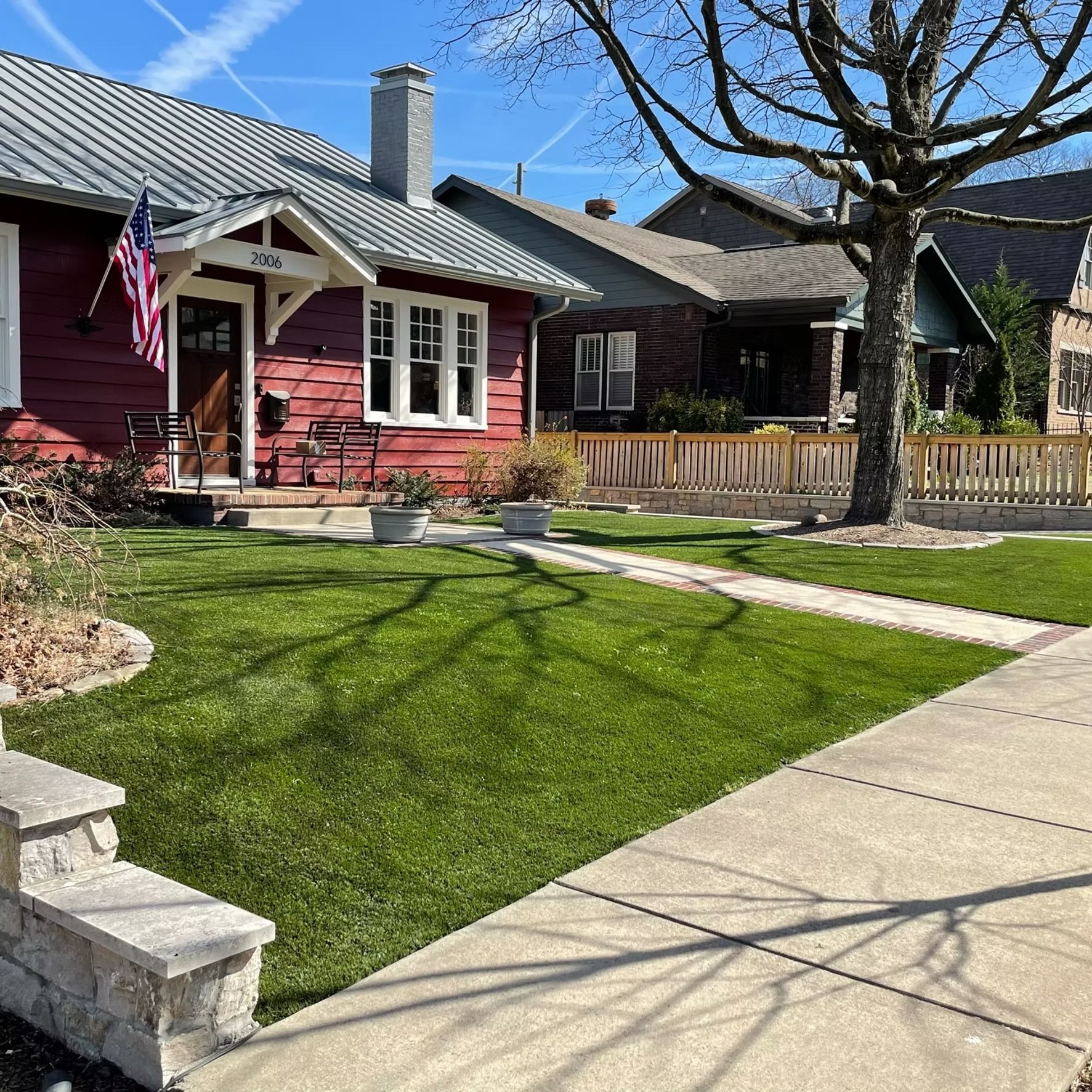 Red house with American flag, green lawn, sidewalk, and neighboring homes.