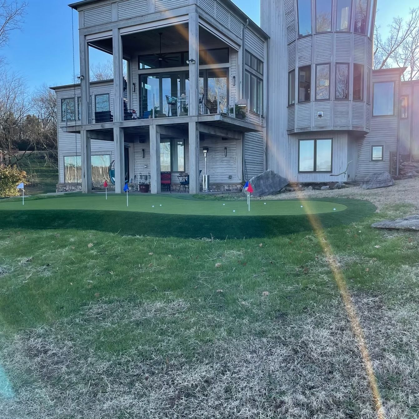 A house with a balcony overlooking a putting green with flags.