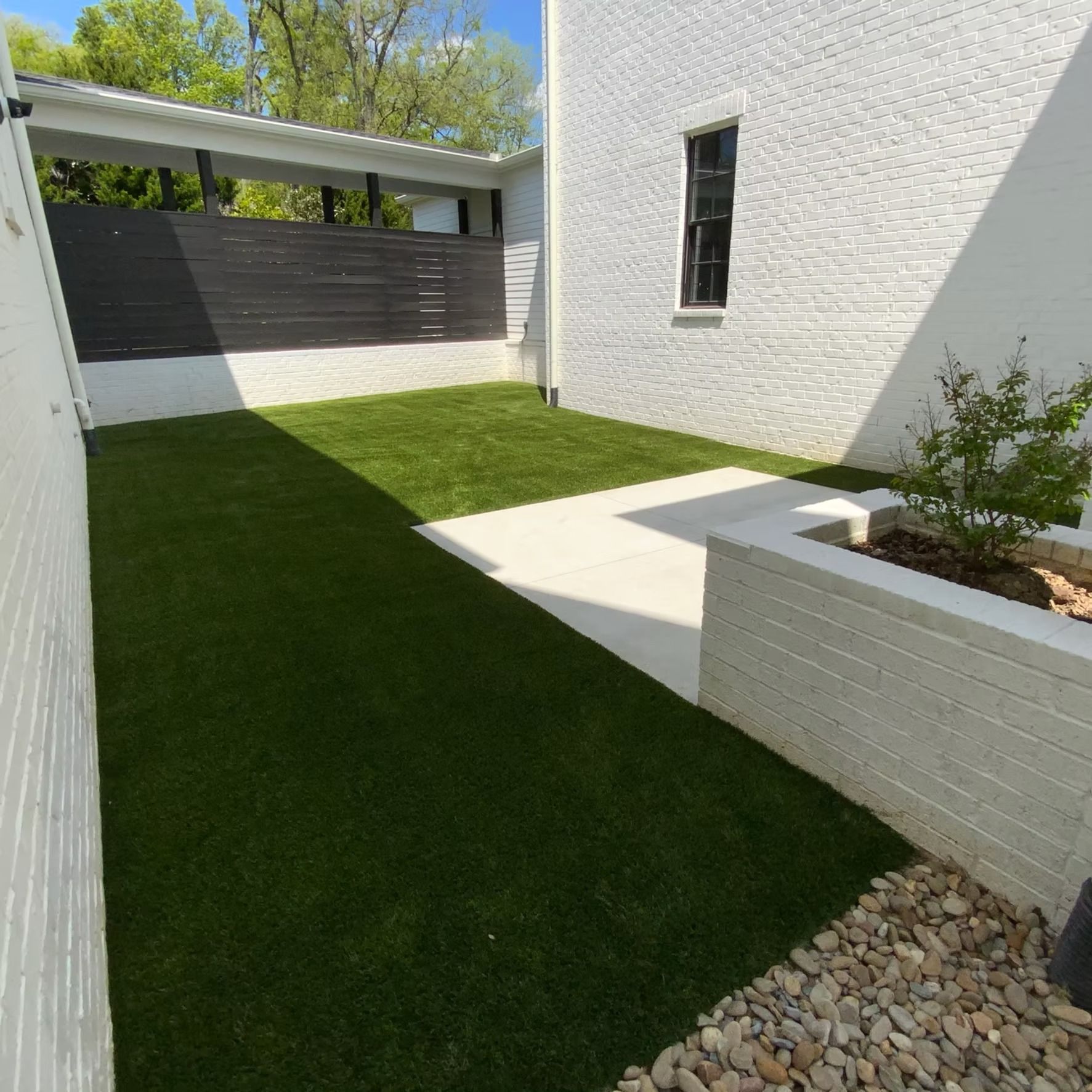 A small backyard with green turf, white brick walls, and a black fence.