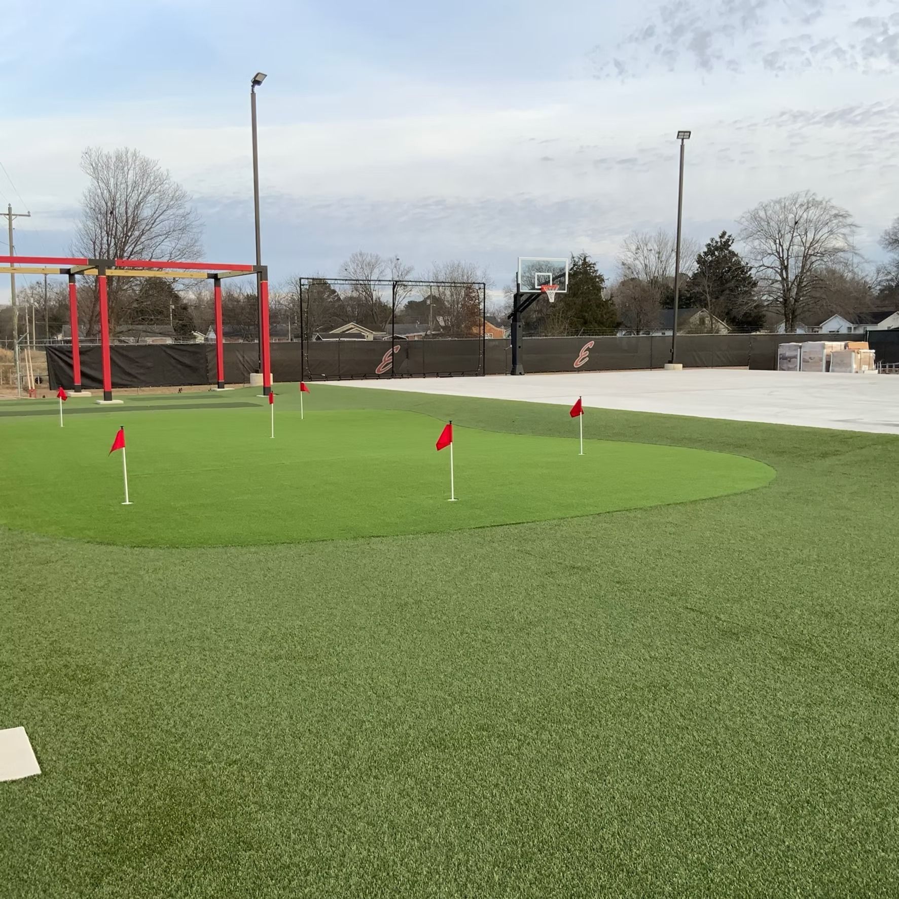 Golf putting green with red flags, basketball hoop, and tall lights.