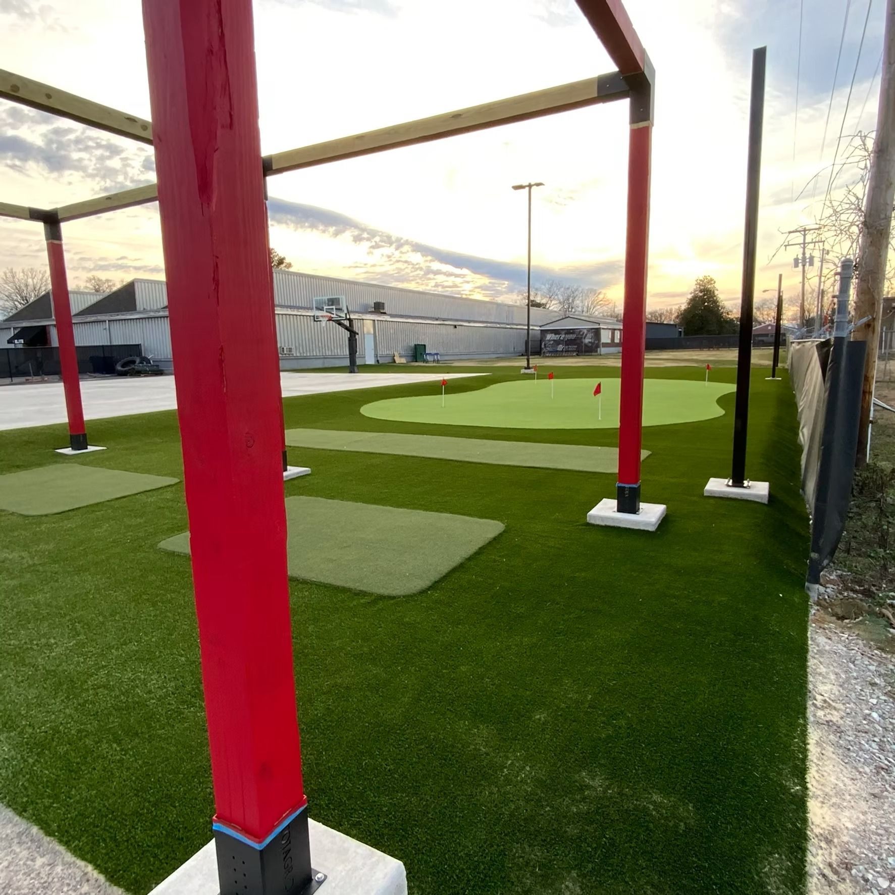 Red-columned structure framing a putting green, synthetic turf. Sunny outdoor setting.
