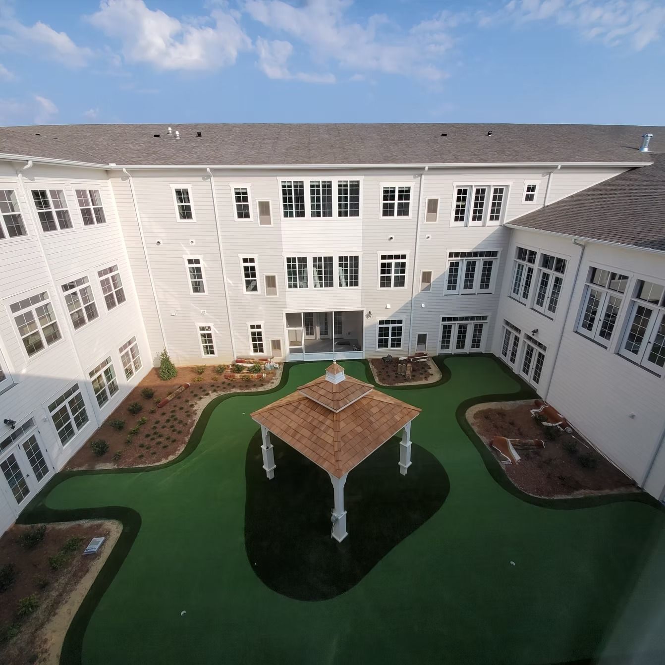 Courtyard with a gazebo, surrounded by a two-story white building, green turf, and landscaping.