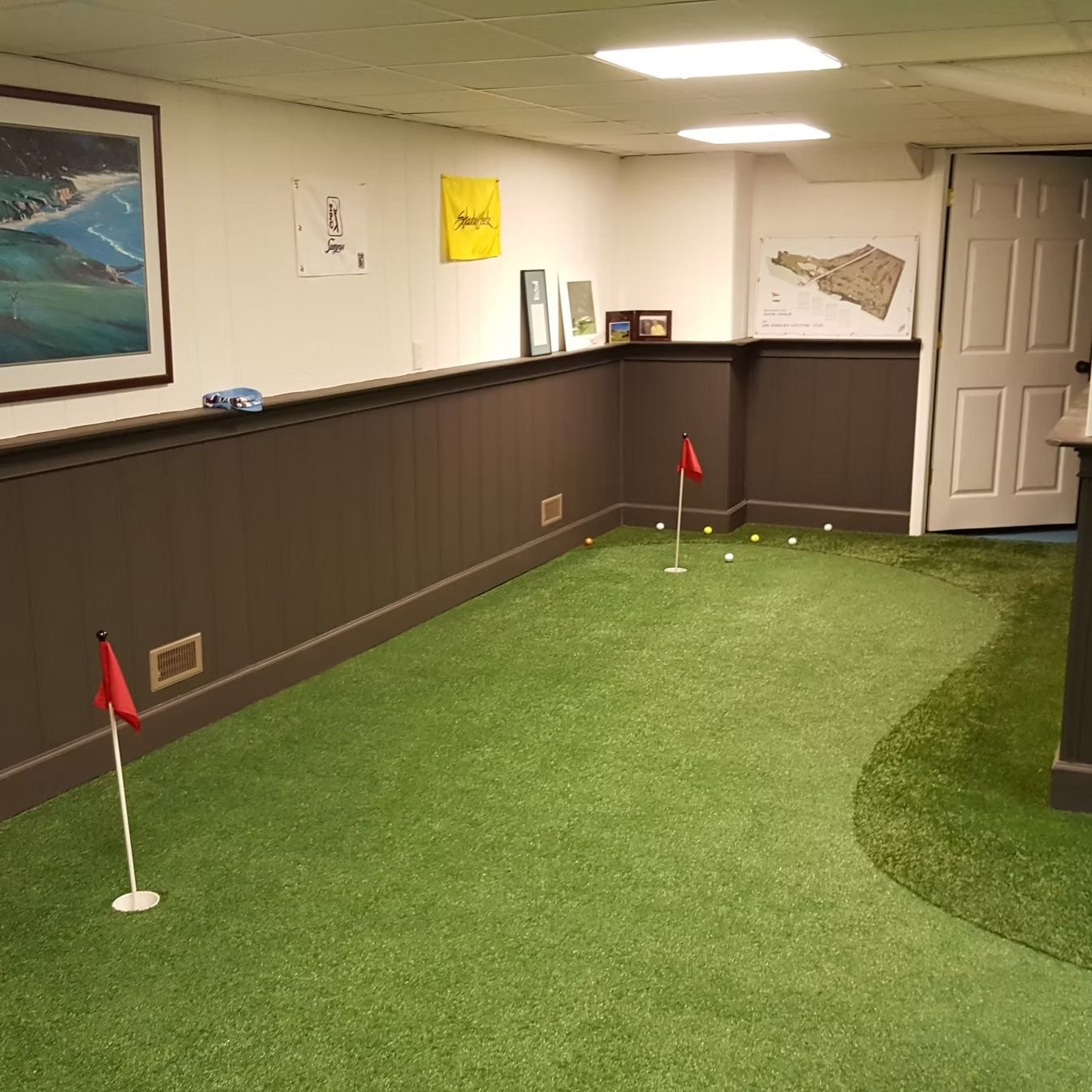Indoor putting green with two red-flagged holes, golf balls, and a dark brown paneled wall.