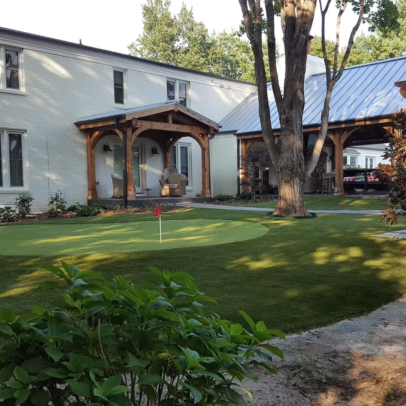 White house with wooden porch and green lawn, including putting green.
