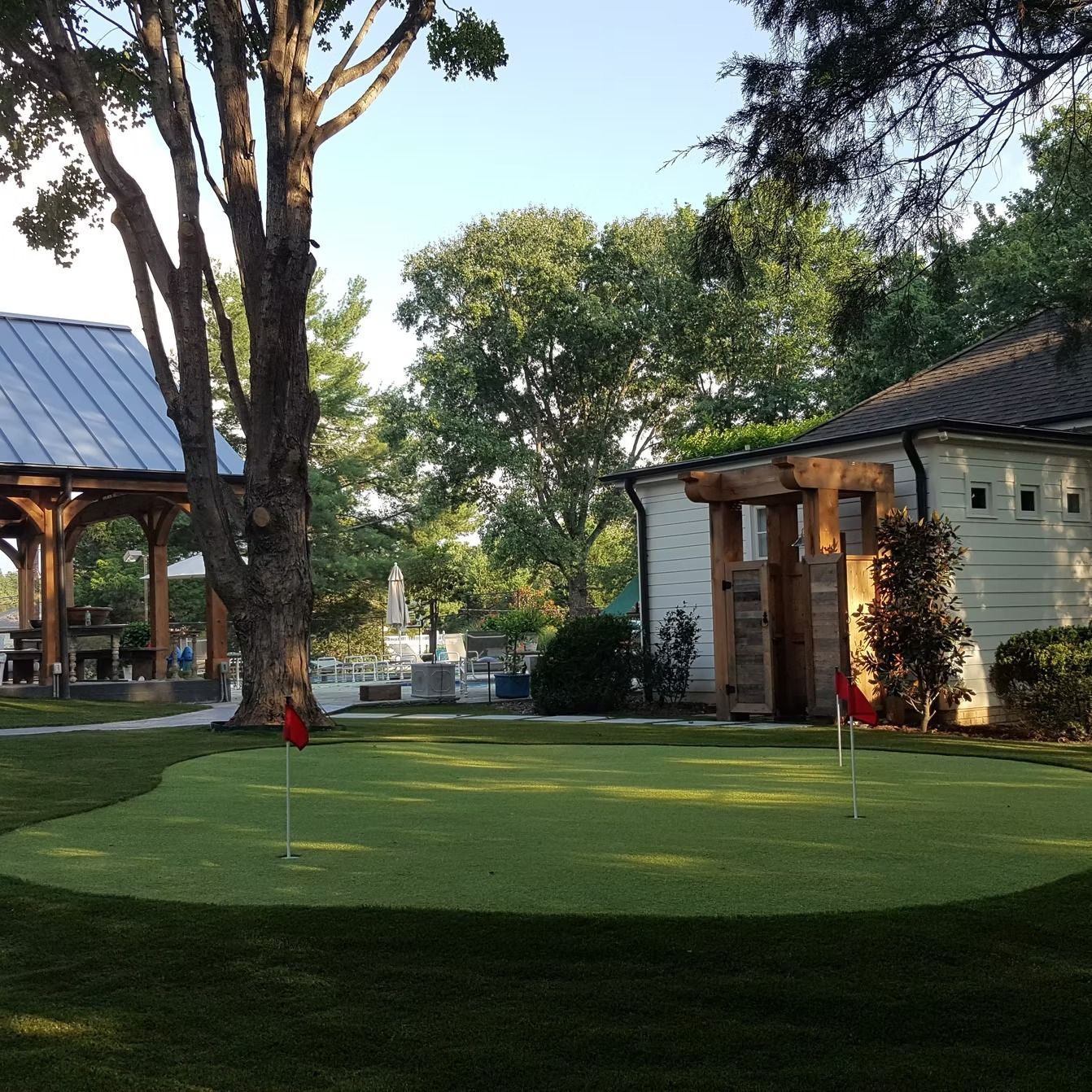 A putting green with red flags, buildings, and trees in an outdoor setting.