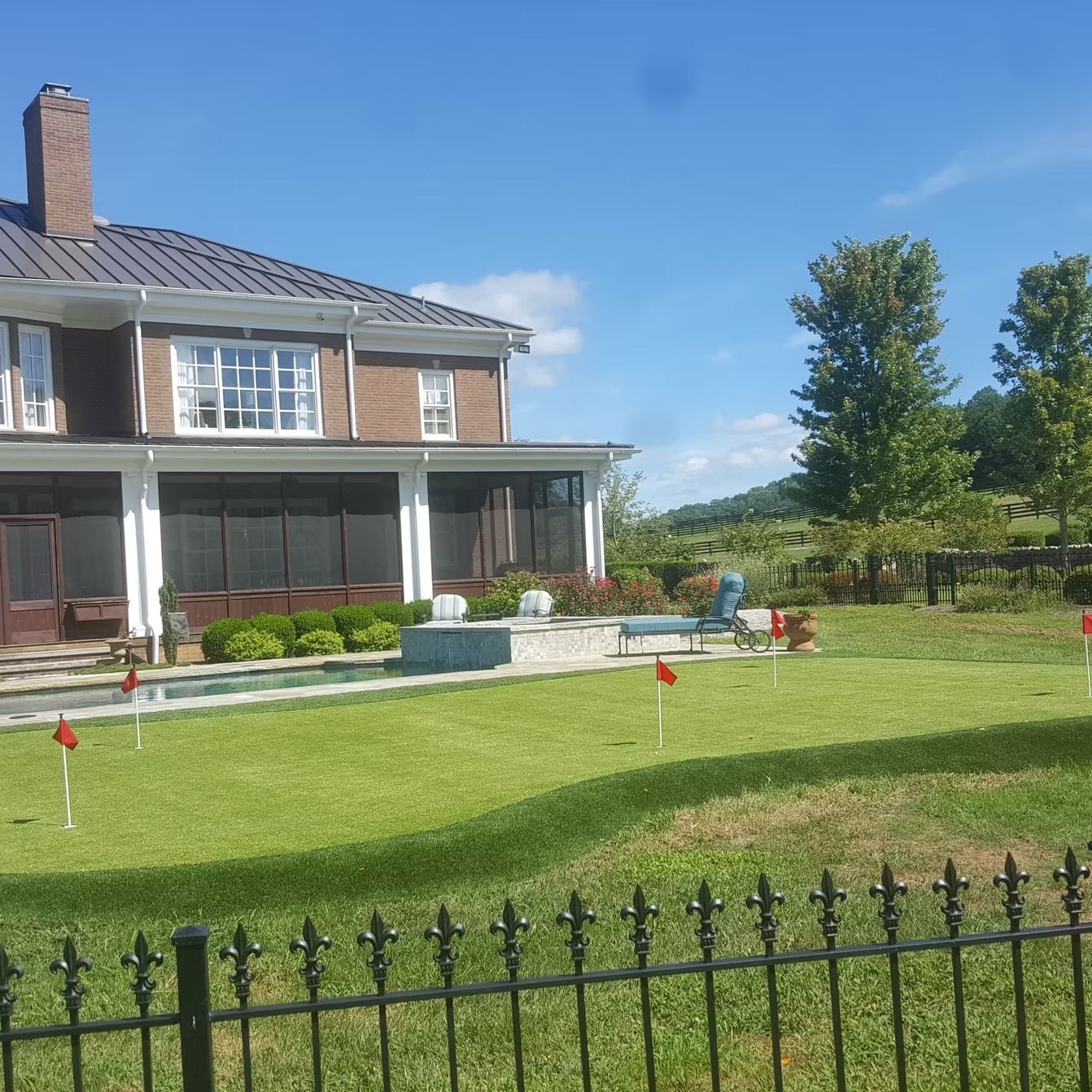 A large brick house with a putting green in the front yard; blue sky and trees in the background.