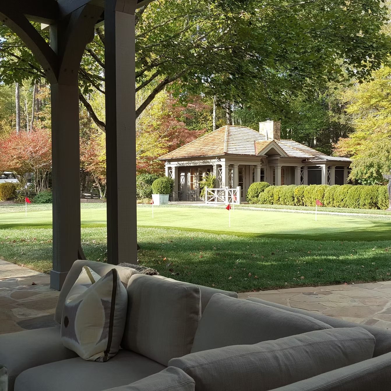 Patio with a sofa overlooking a grassy yard and a small house, trees in the background.