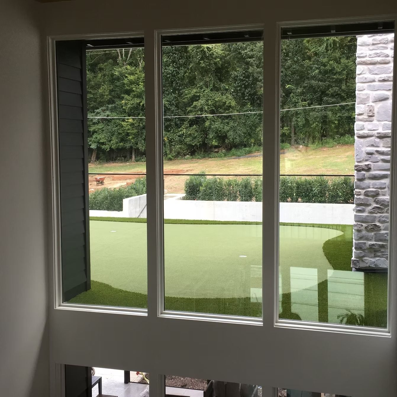Three-pane window overlooking a green putting green and trees. Stone wall to the right.